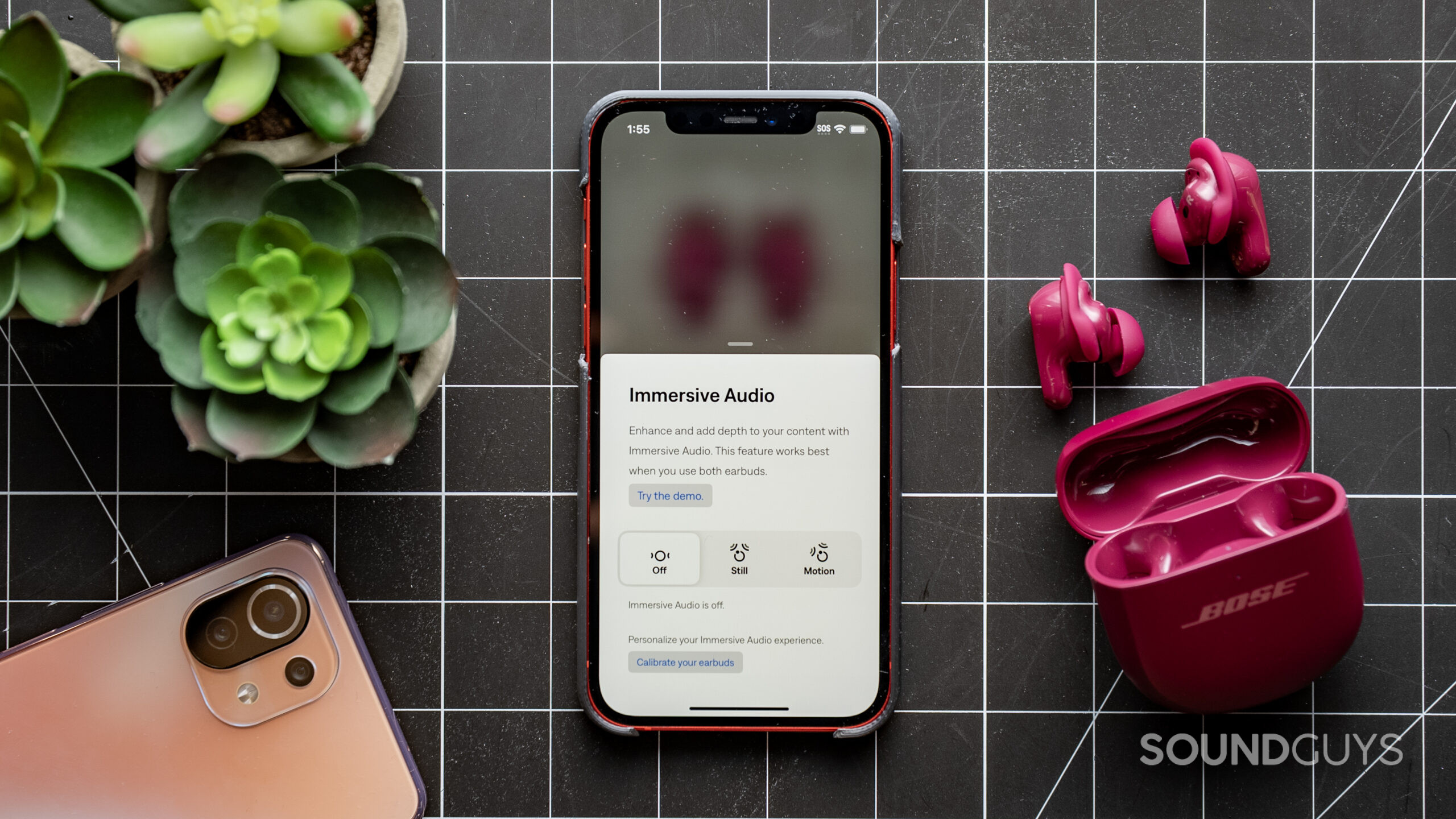A photo of a phone with the Bose app open to the spatial audio screen, showing the deep plum-colored Bose QuietComfort Ultra Earbuds on a table nearby.