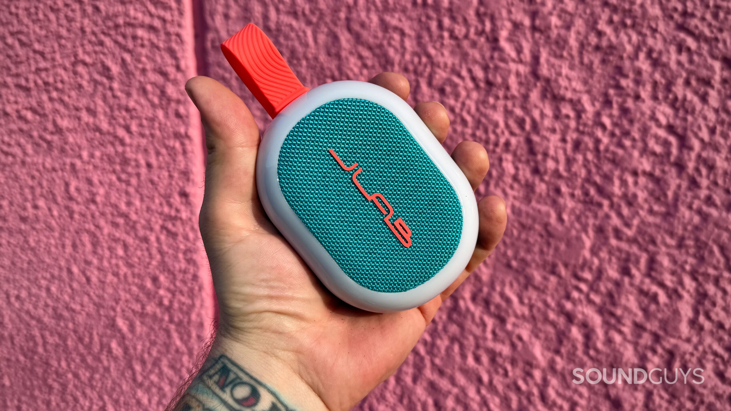 A hand holds a JLab Pop Party with a pink background.