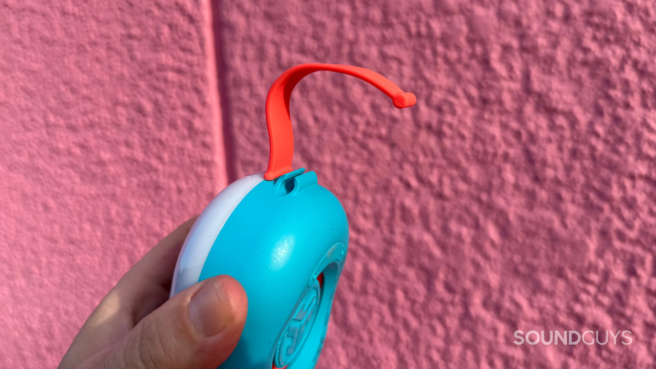 a hand holding the A JLab Pop Party, showing its attachment strap.