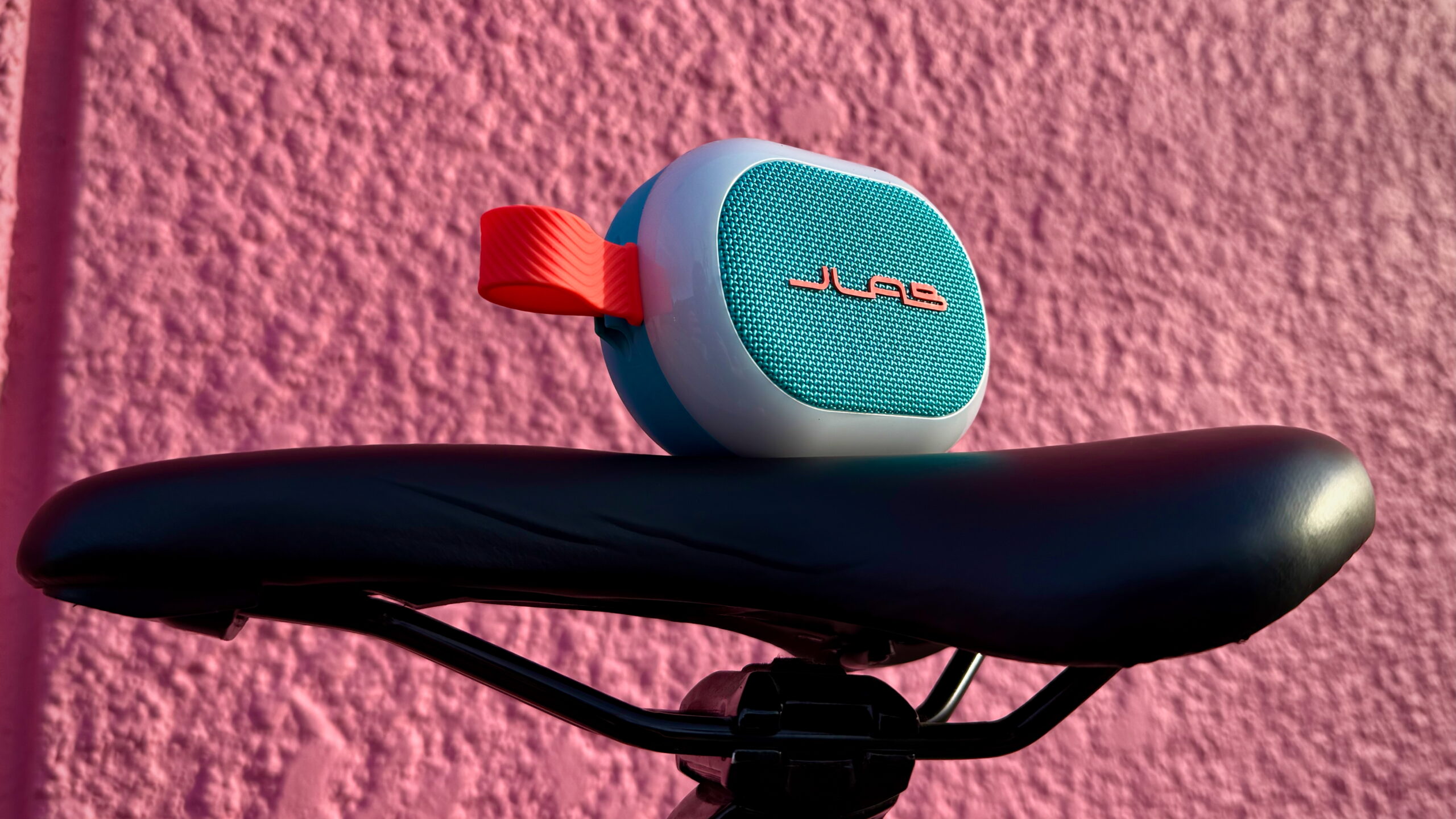 JLab Pop Party - 7 A JLab Pop Party placed on a bike seat with a pink background.