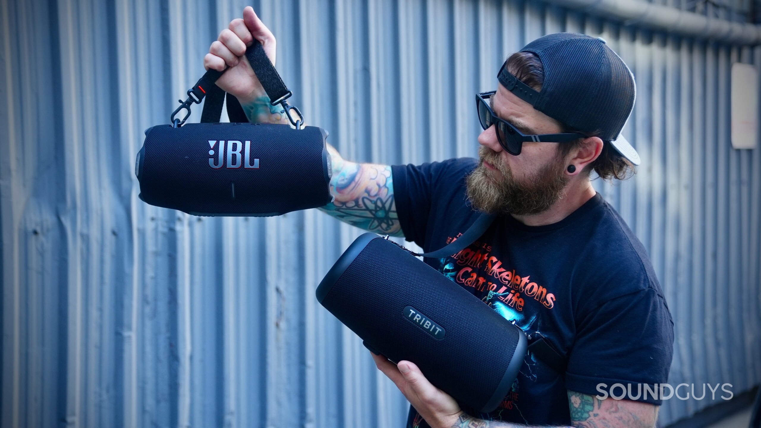 A man holding a Tribit StormBox Lava and JBL Xtreme 4