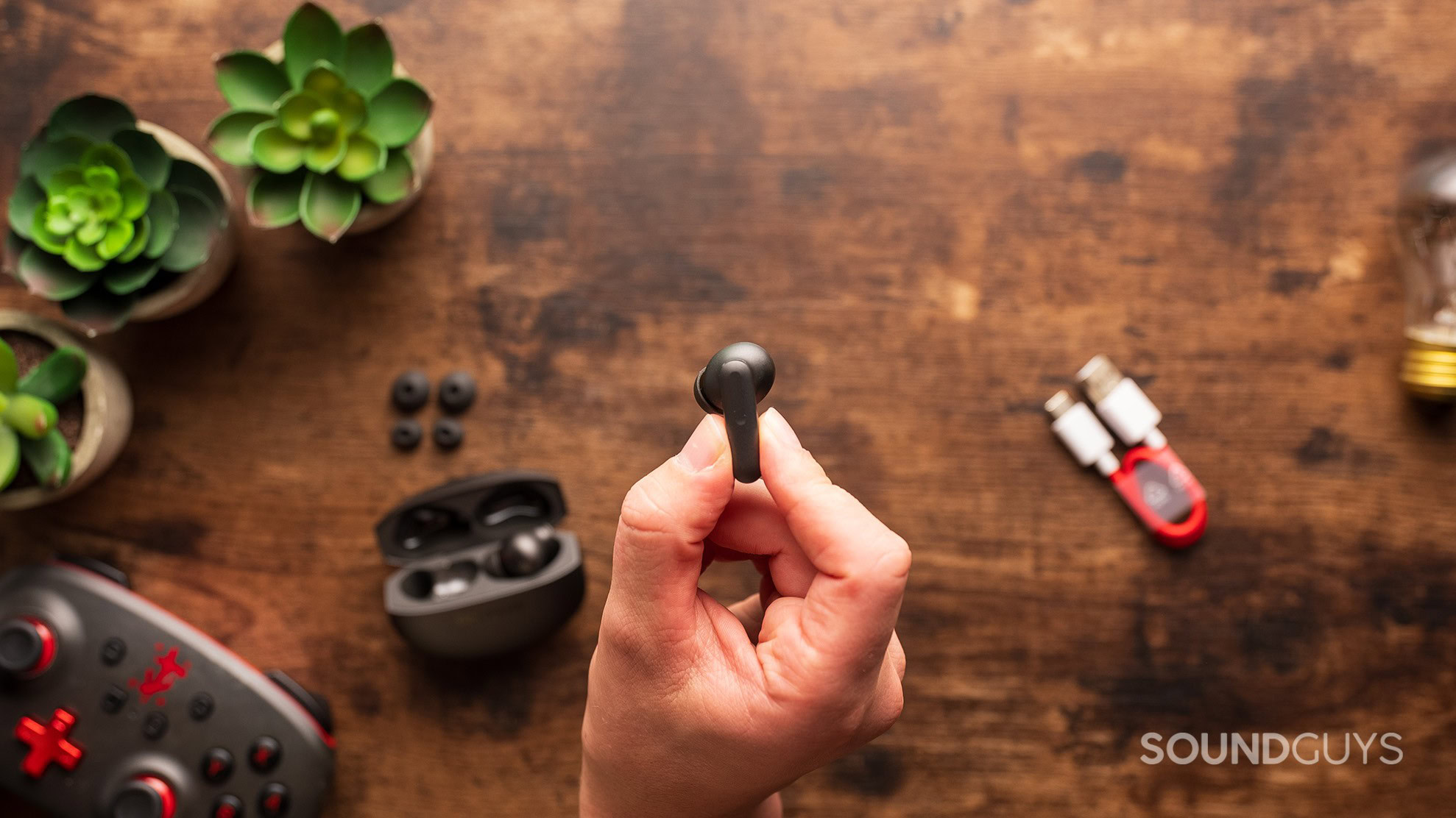 A hand holds a OnePlus Buds 4 earbuds.