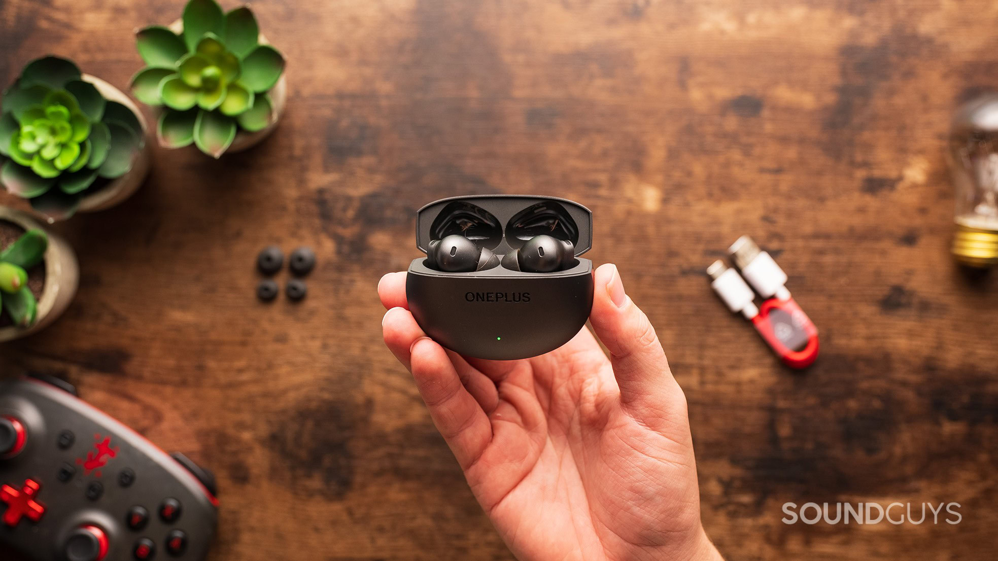 A hand holds the OnePlus Buds 4 earbuds in their case.