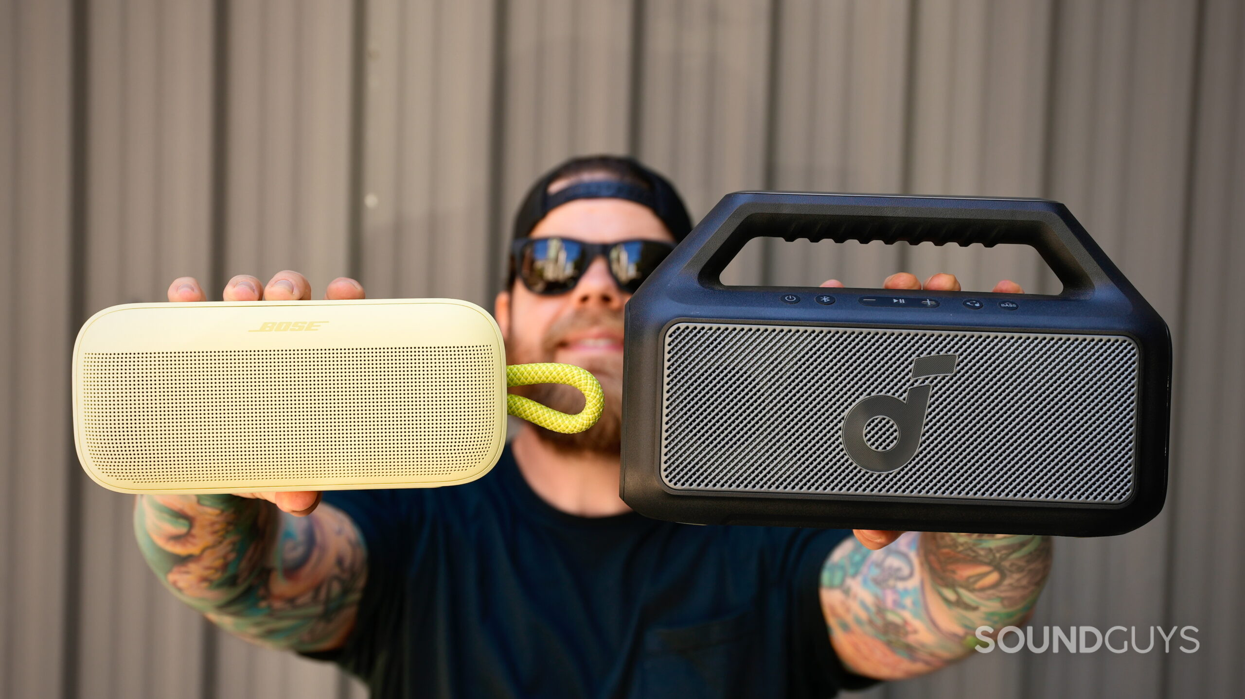 SL Plus vs Boom 2 - 1 A man holds a Bose SoundLink Plus and Soundcore Boom 2 out in front of his face.