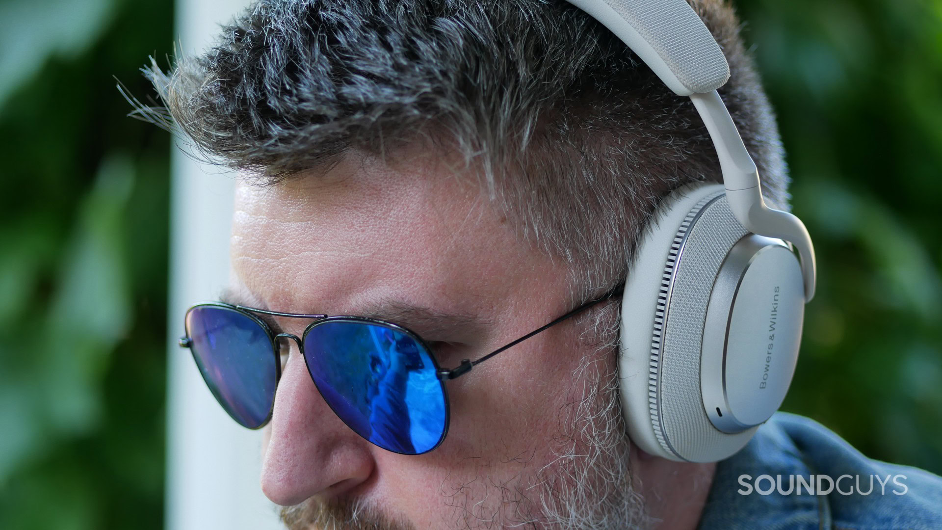 bower-and-wilkins-px7-s3-wear A man wearing sunglasses wears the Bowers & Wilkins PX7 S3 in front of leaves.
