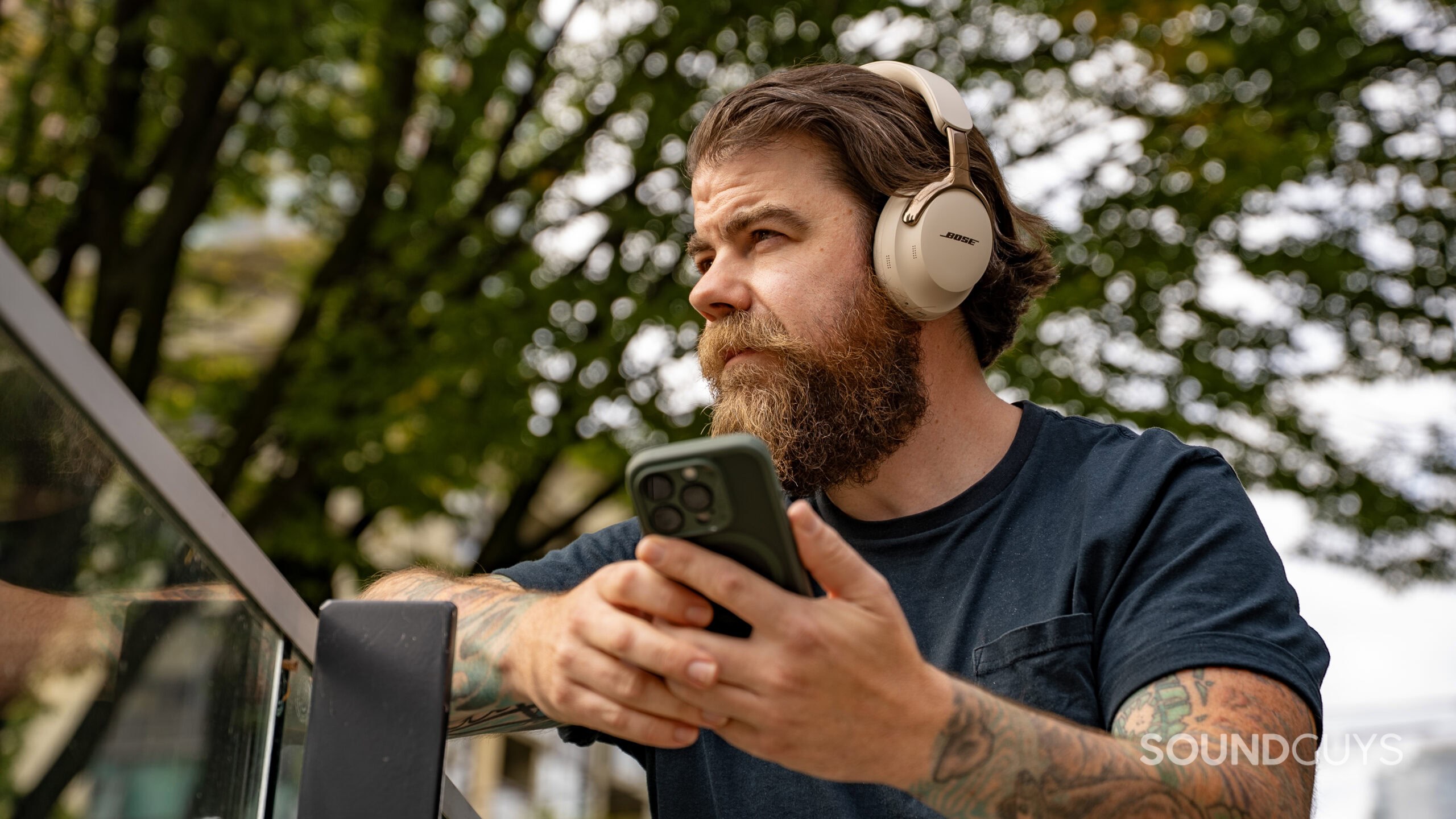 A tattooed man operates a smartphone while wearing the Bose QuietComfort Ultra (2nd Gen.)