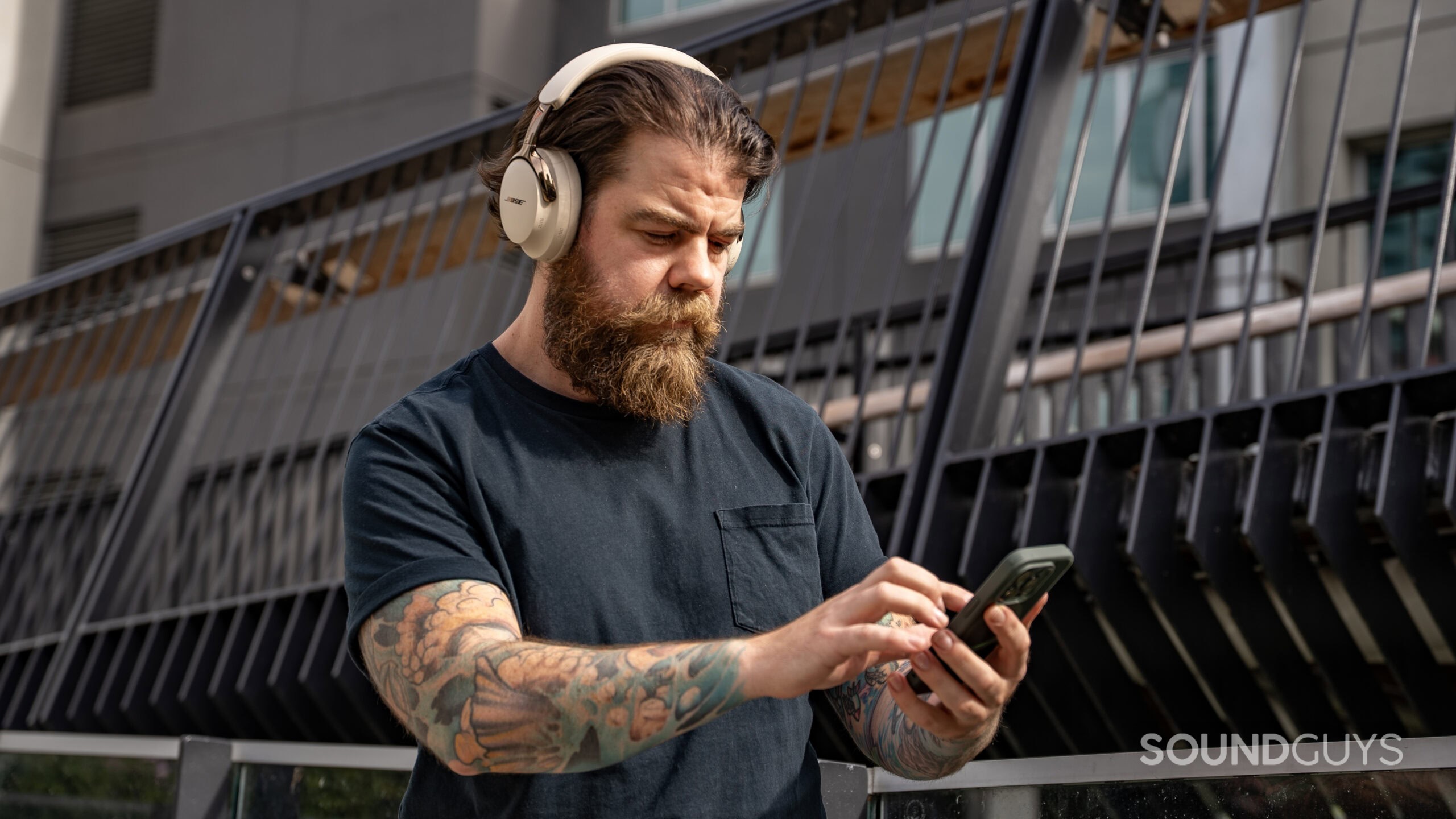 Bose-QuietComfort-Ultra-Headphones-2nd-Gen-man-on-phone-looking-right A tattooed man operates a smartphone while wearing the Bose QuietComfort Ultra (2nd Gen.)