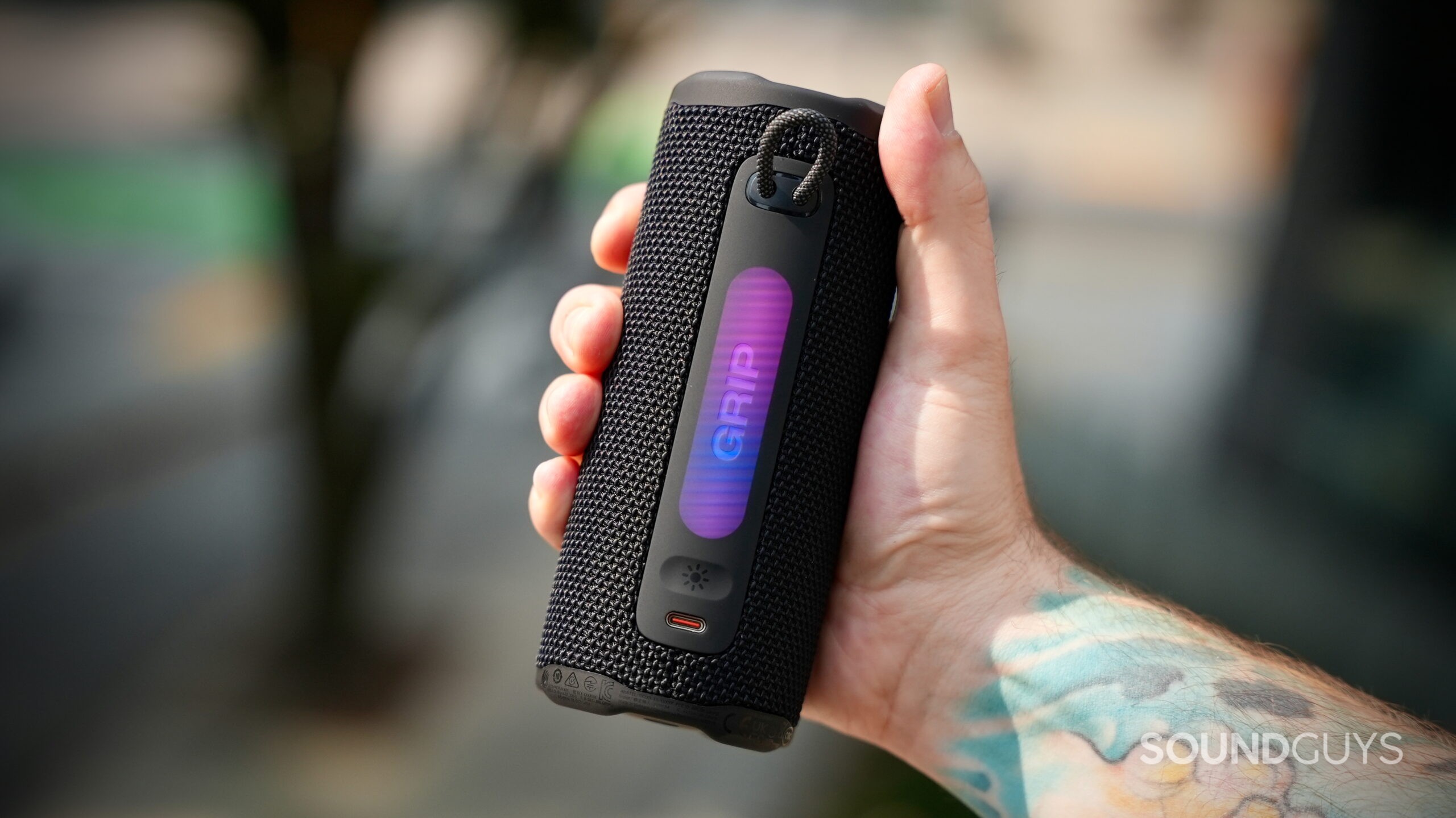A JBL Grip speaker being gripped by a hand, showing it's rear ports and light