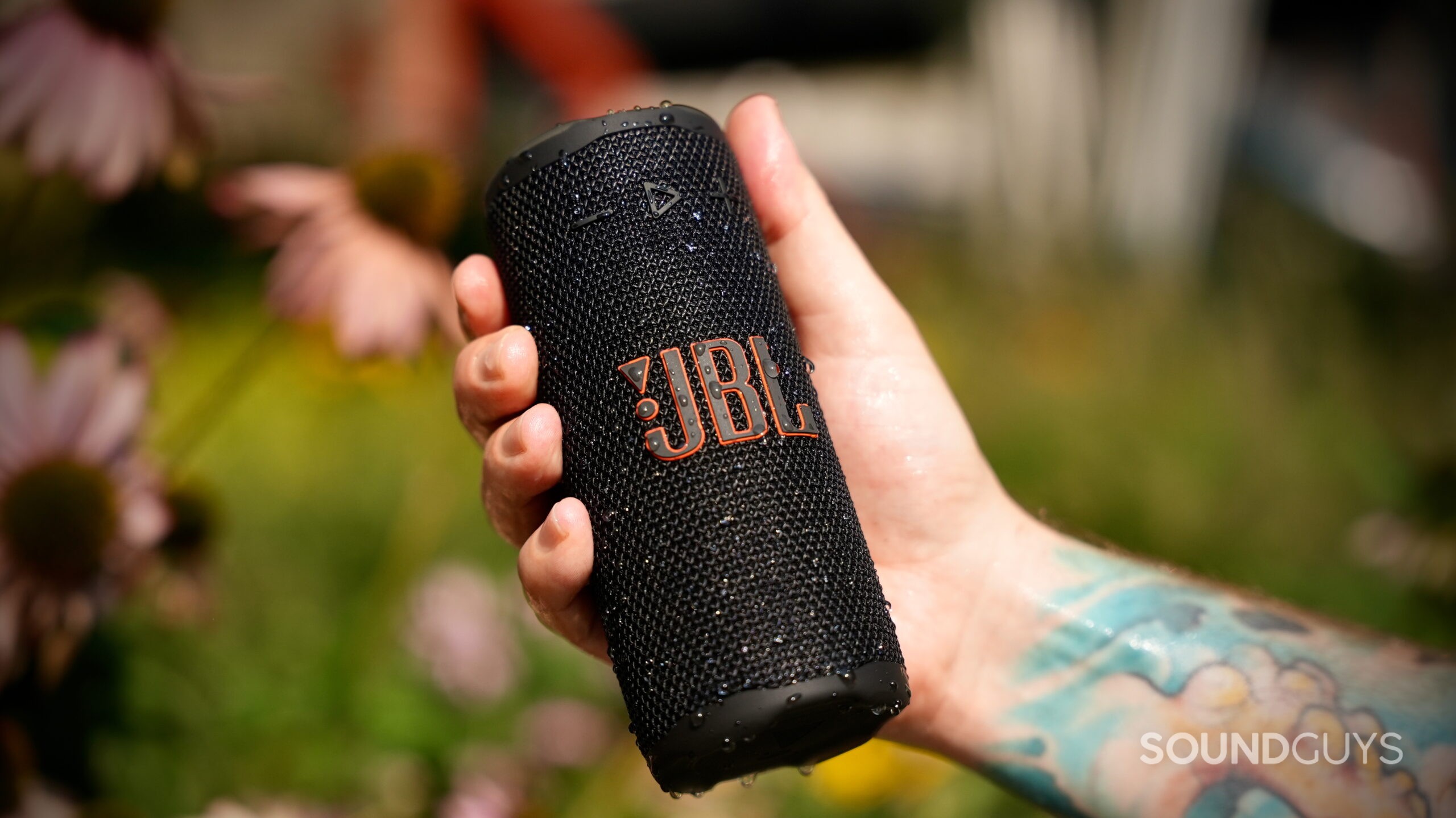 A hand holds a wet JBL Grip speaker