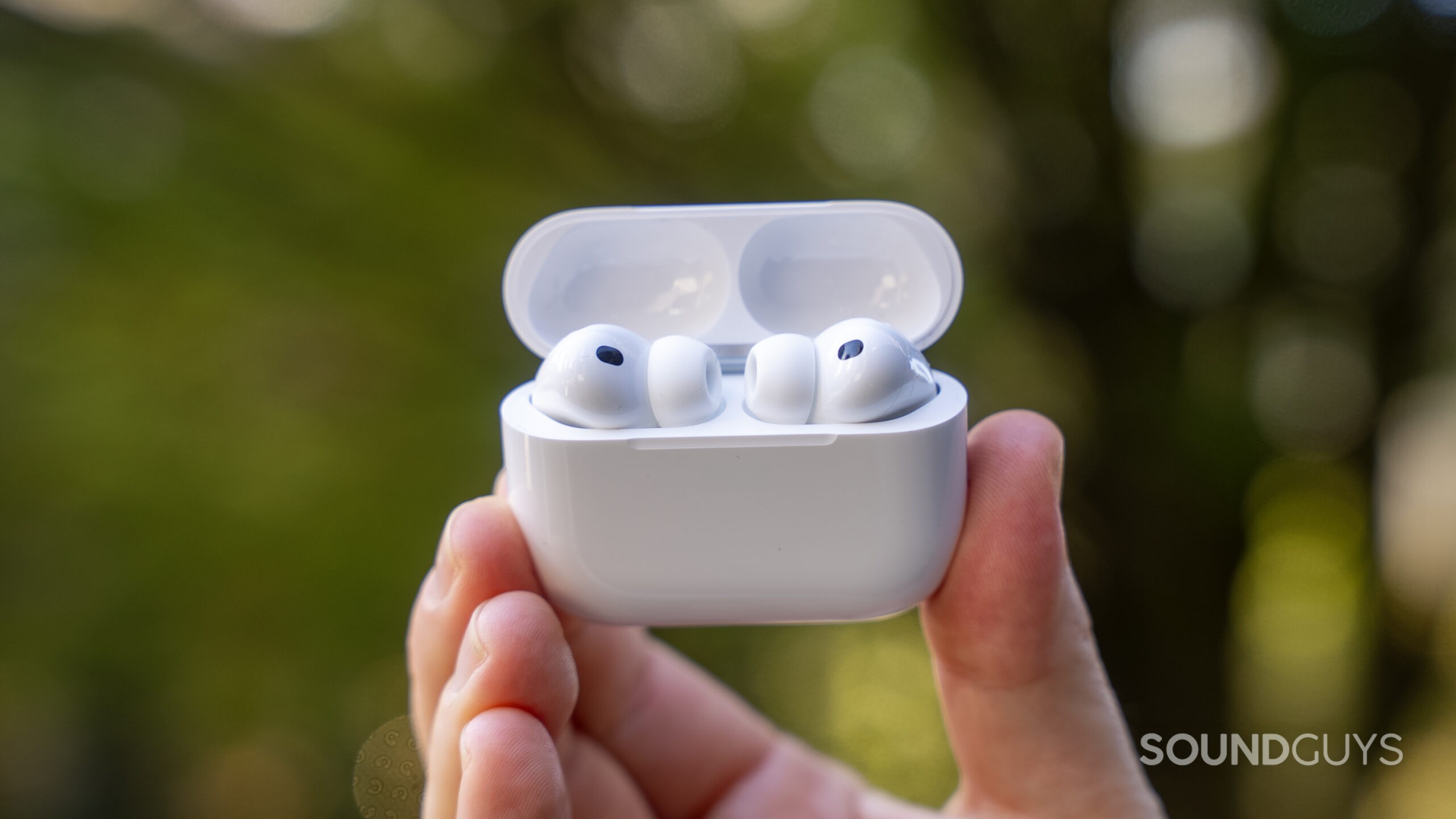 AirPods Pro 3 in hand outside in front of a bush.
