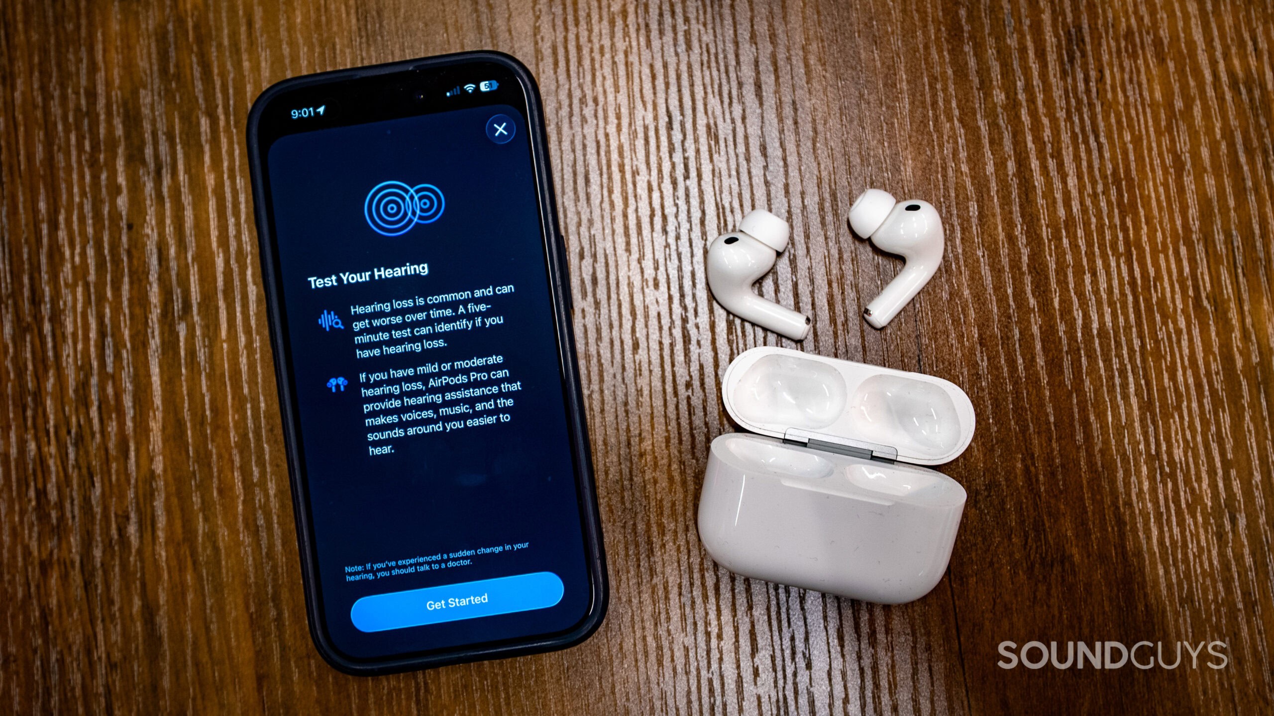 Apple AirPods Pro 3 on wooden table next to iPhone showing Apple Hearing Test