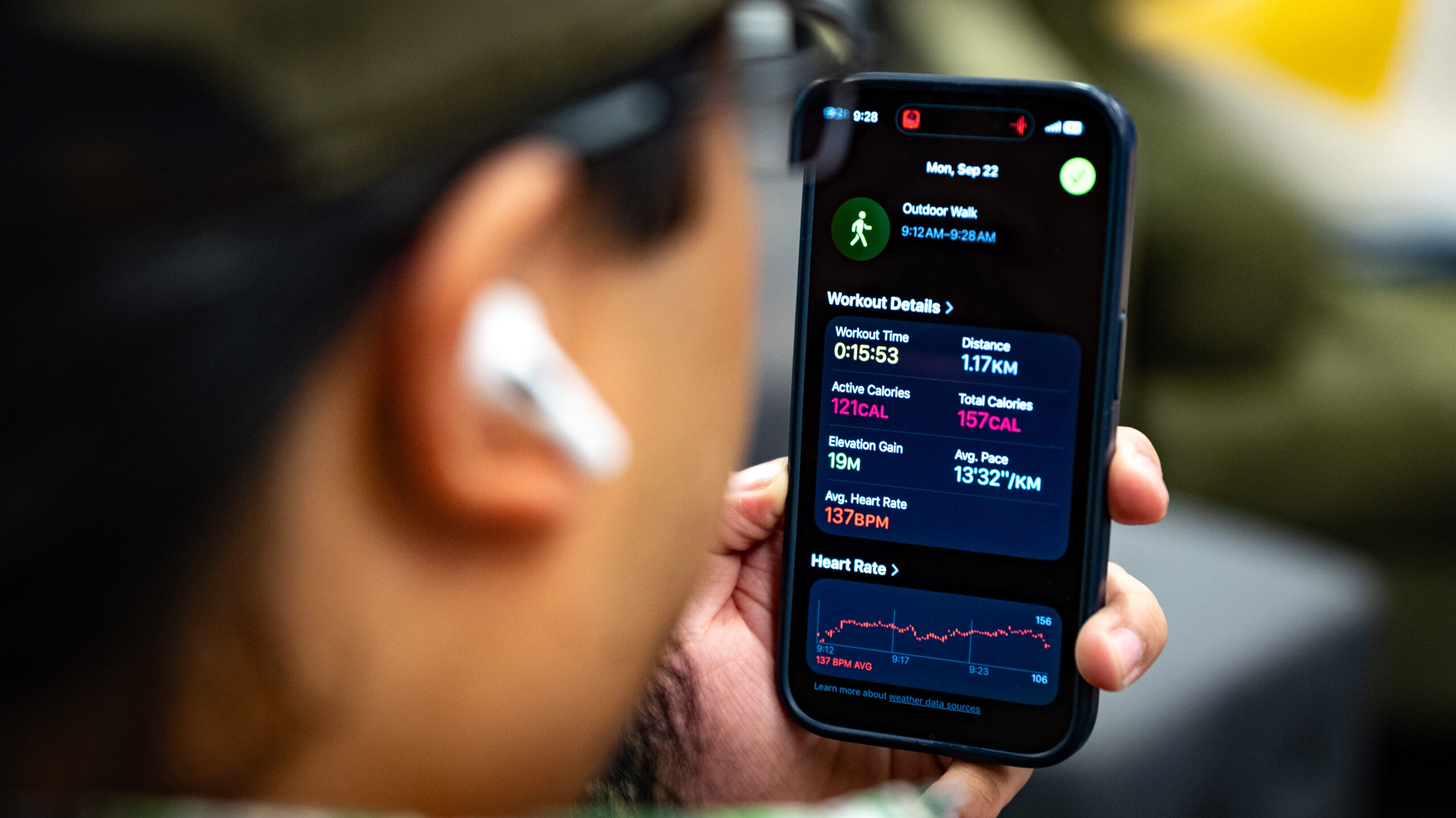 AirPods Pro 3 in man's ear as he looks into iPhone showing workout summary