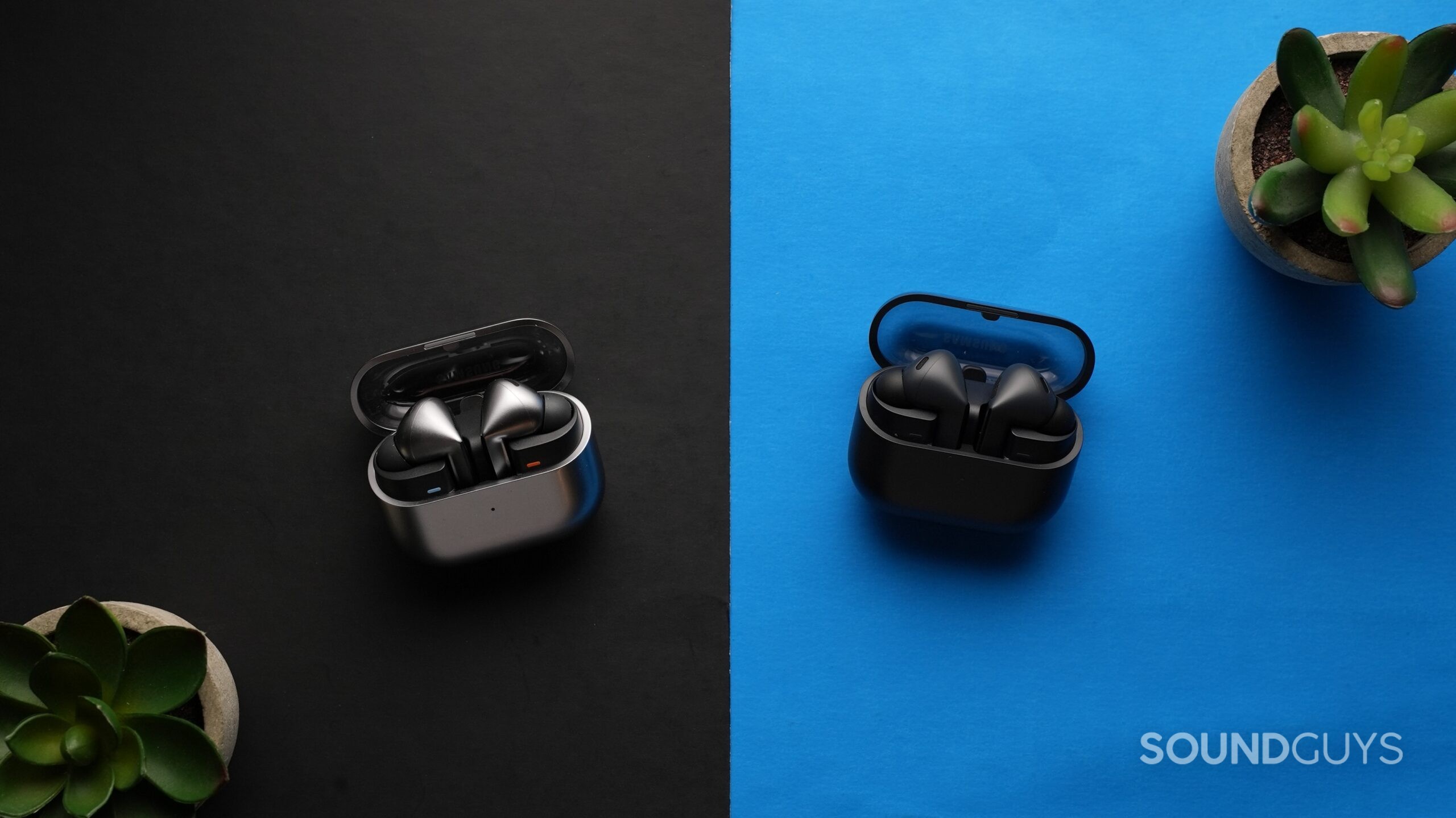 The Samsung Galaxy Buds 3 Pro sit on a table next to the Galaxy Buds 3 FE, surrounded by plants.
