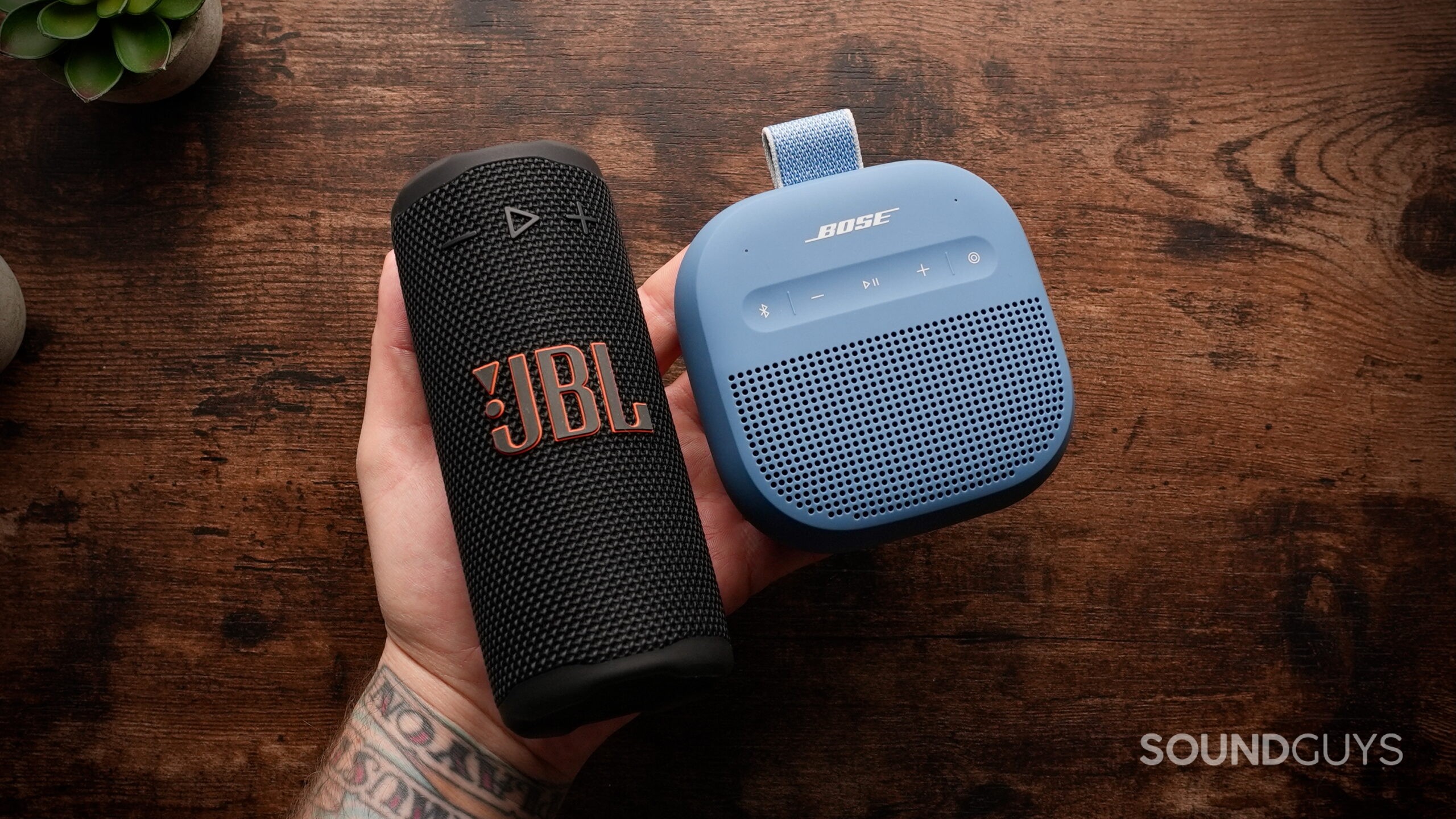 Grip Vs Micro Bose - 2 A hand holding the JBL Grip and the Bose SoundLink Micro (2nd Gen)