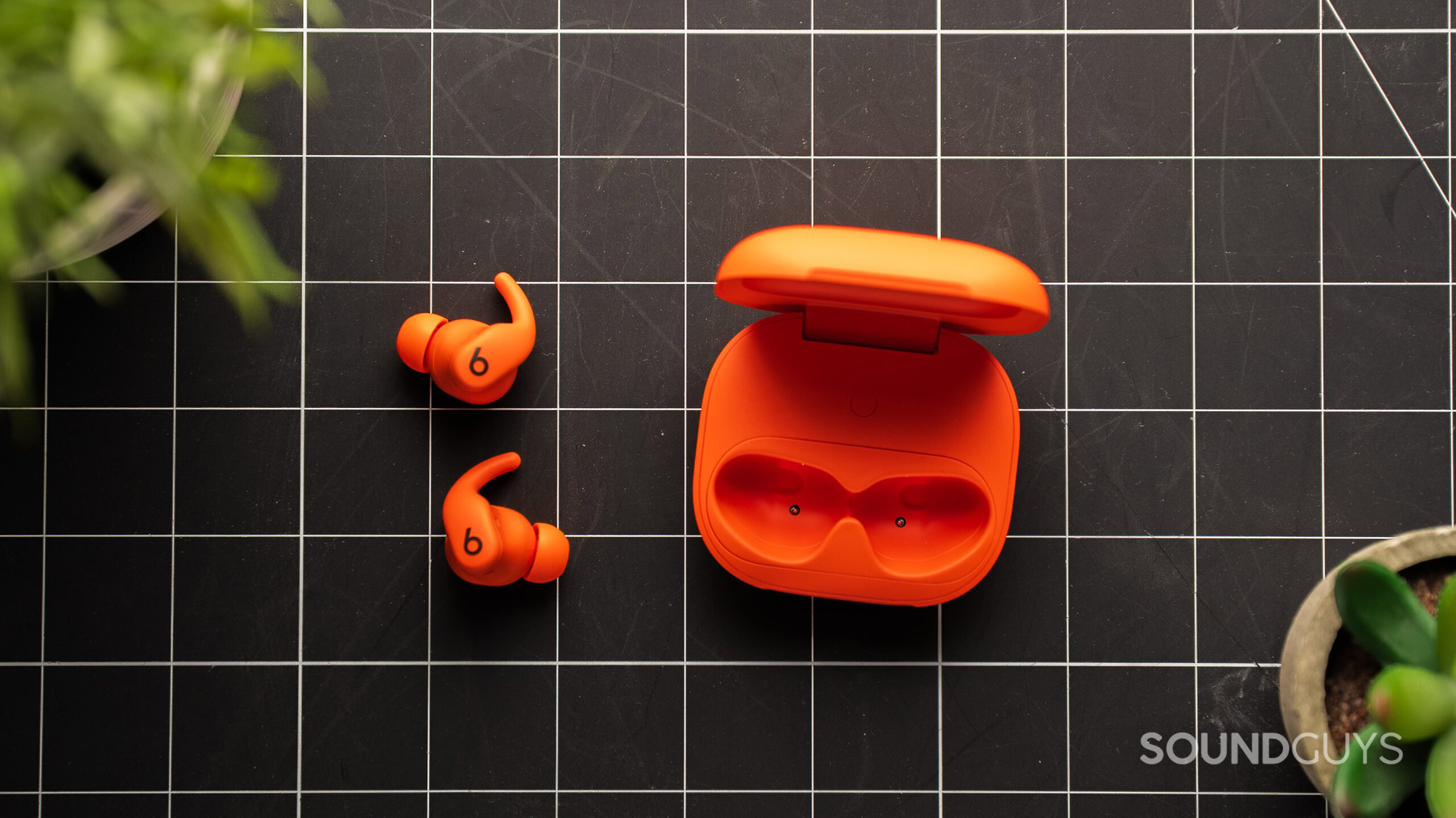 Powerbeats Fit earbuds next to case Powerbeats Fit earbuds in orange on a table.