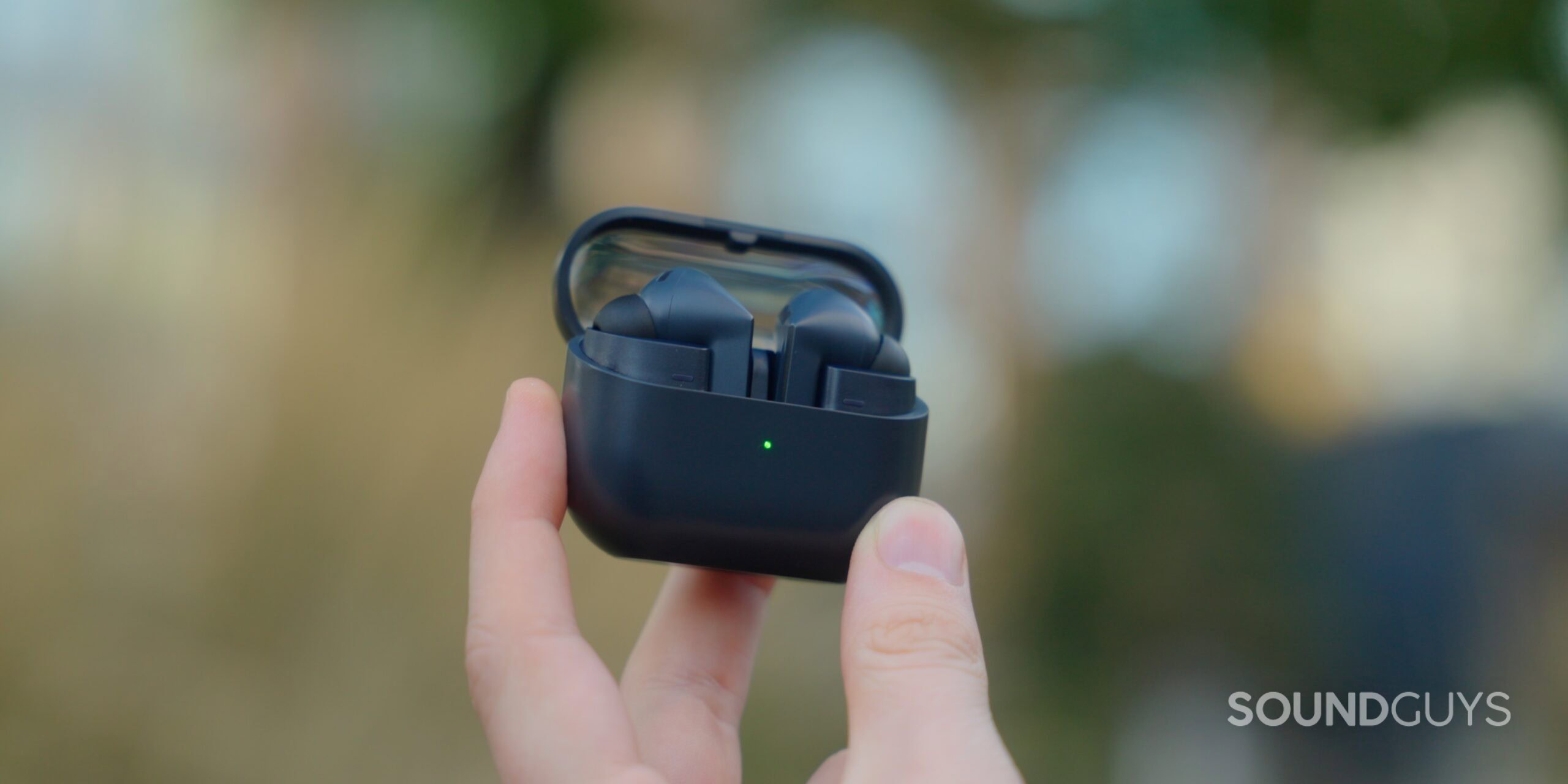 A hand holds up the Galaxy Buds 3 FE case in the air. The case is open.