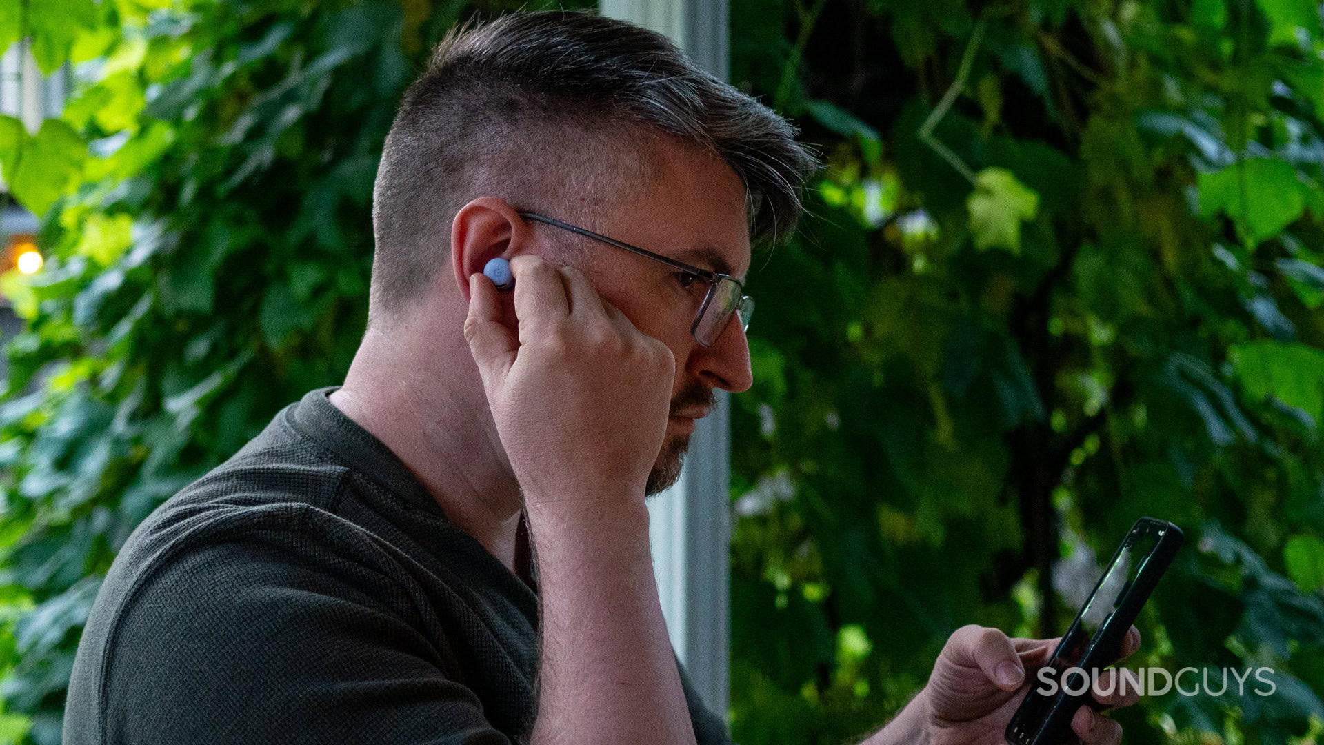 google-pixel-buds-2a-wear A man wears the Google Pixel Buds 2a while holding a smartphone outdoors.