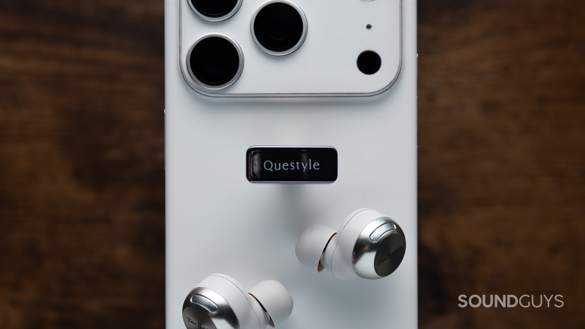 Questyle QCC Dongle Pro on an iPhone, with earbuds underneath.