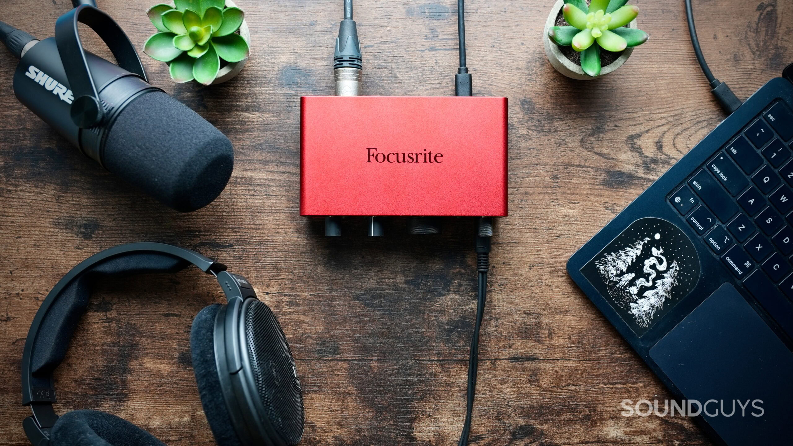 Top down photo of a Focusrite Interface connected to a laptop, Sennheiser headphones, and a Shure mic.