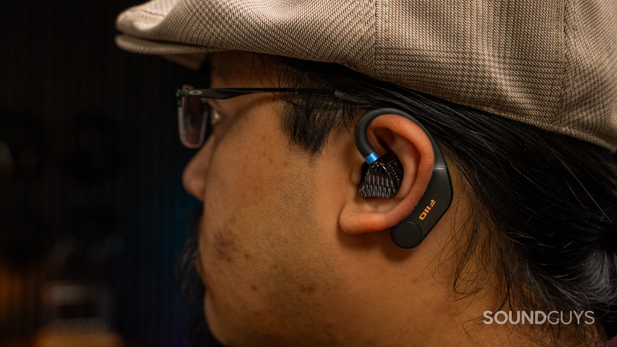 A man wearing a cap with a wireless bluetooth earbud that goes over the ear.