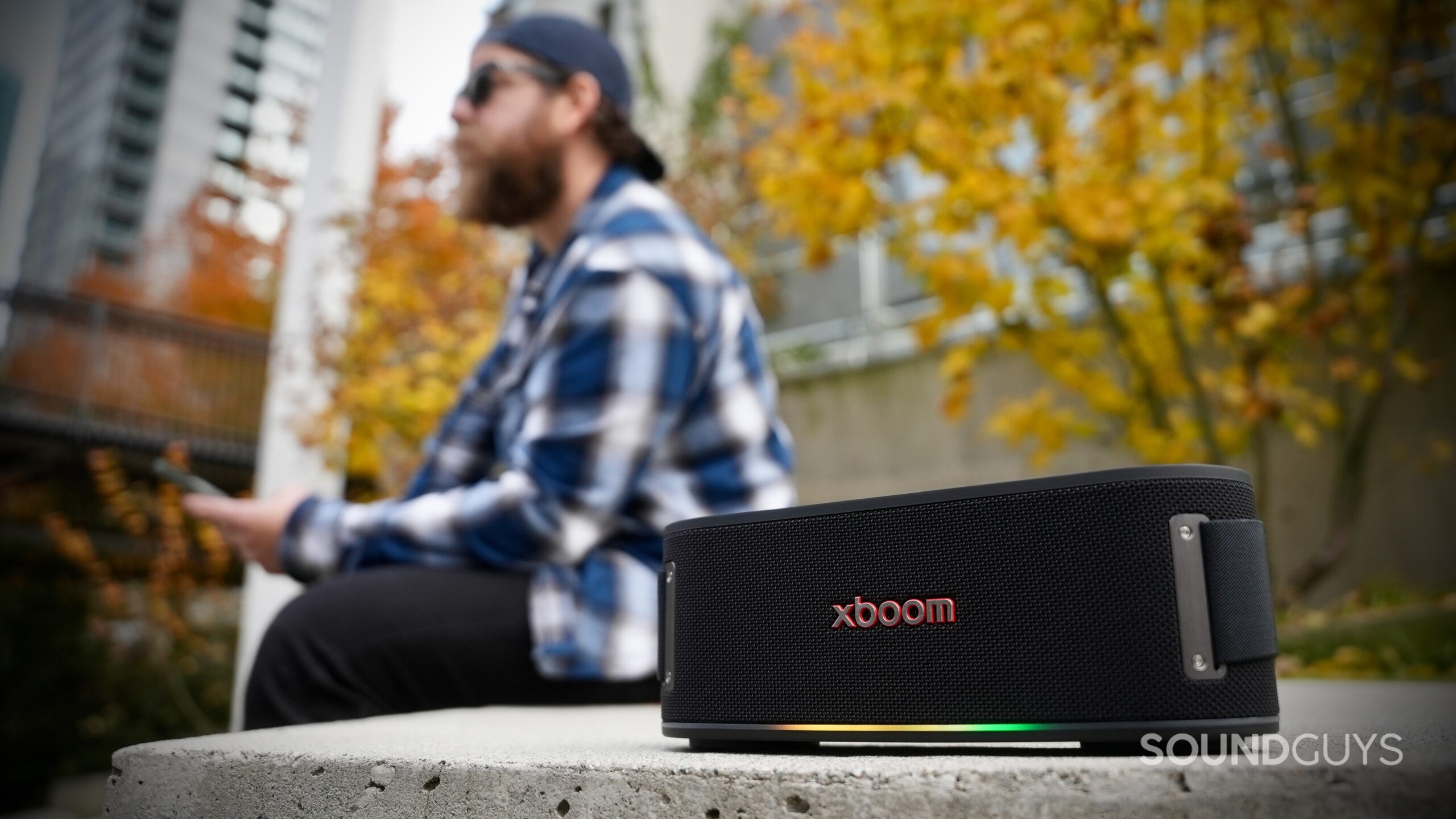 LG xboom Bounce - 1 A man sitting next to an LG xboom Bounce speaker outside.