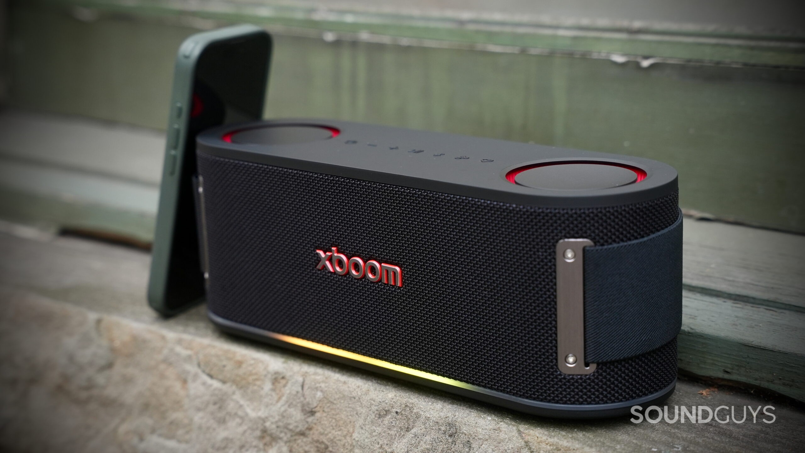 An LG xboom Bounce speaker placed on a concrete window sill with an iPhone leaning against it.