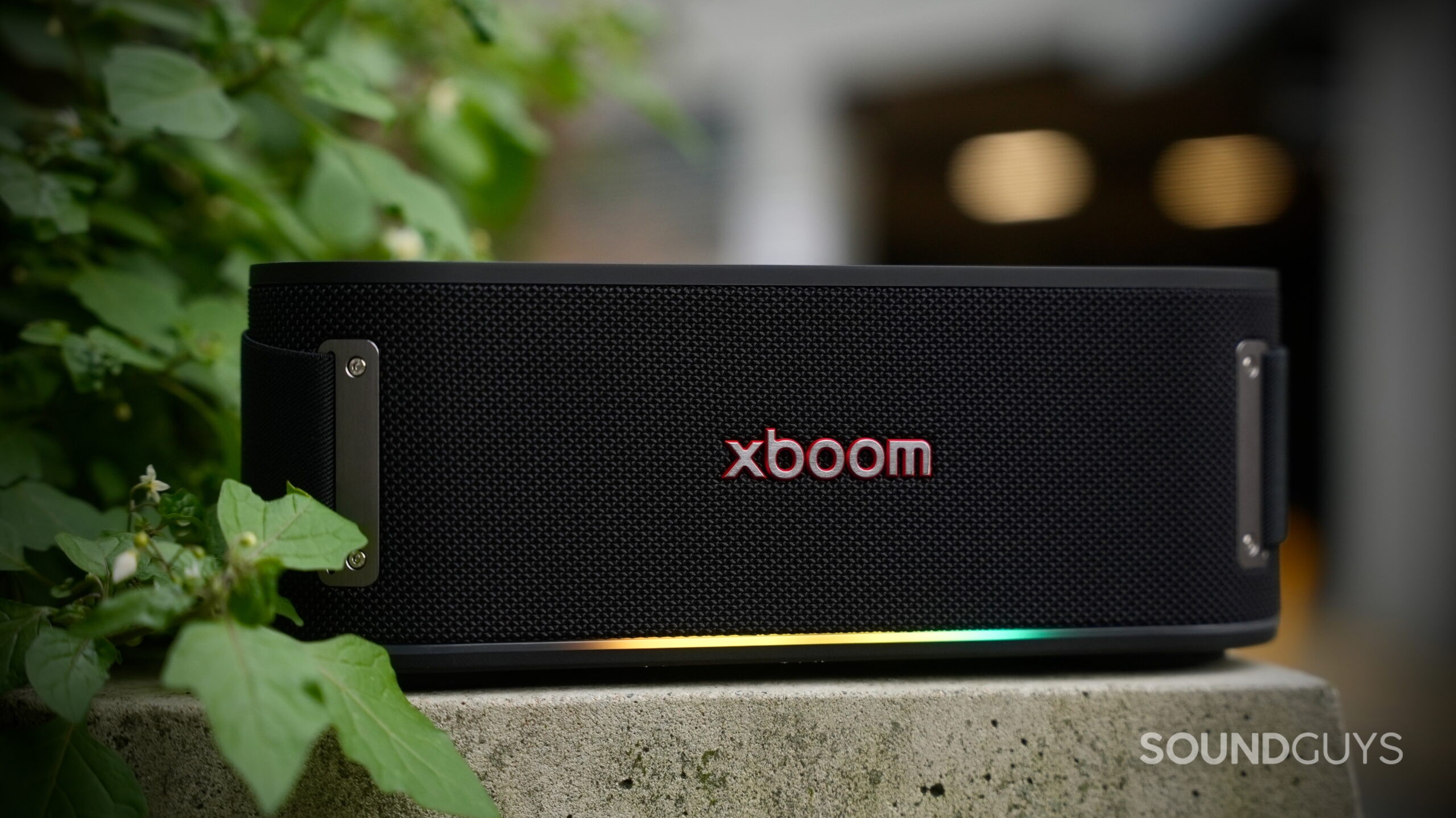 LG xboom Bounce - 8 An LG xboom Bounce speaker placed on a concrete slab with some greenery at the side.