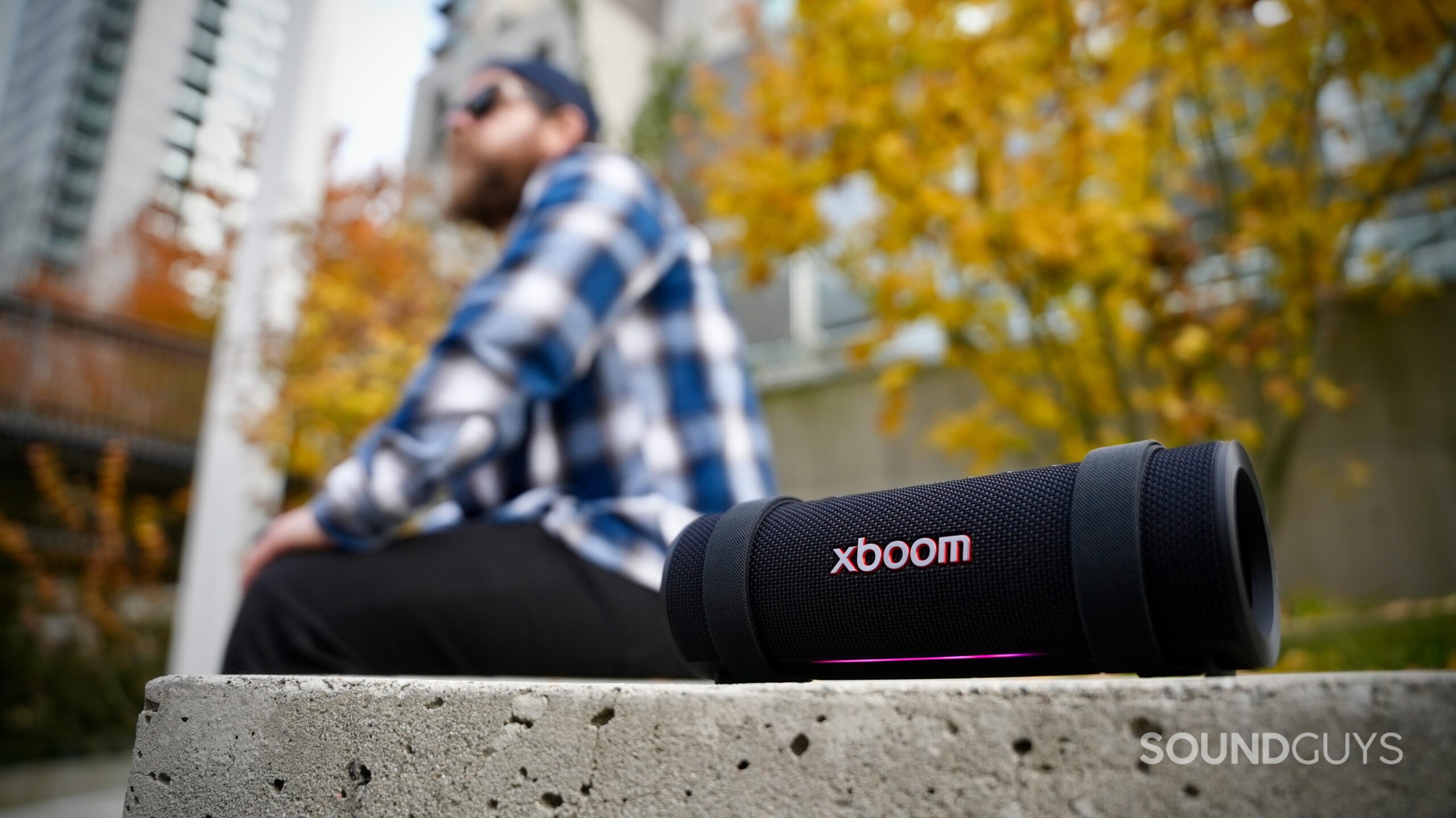 LG xboom series - 1 An LG xboom Grab speaker placed next to a man in sitting down in the city.
