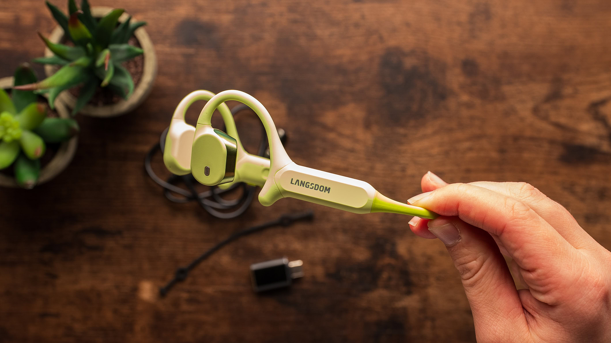 A hand holds the Langsdom AirWave Max headphones.