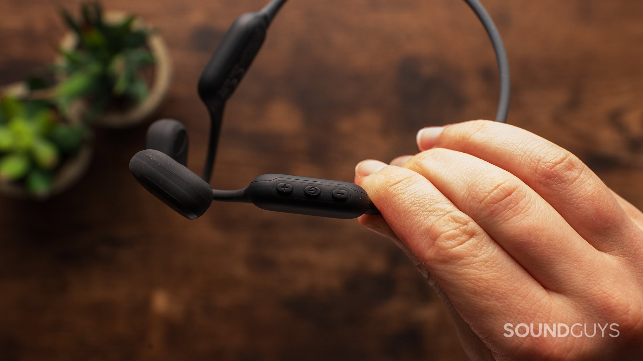 A hand holds the AirWave Pro headphones showing the controls.
