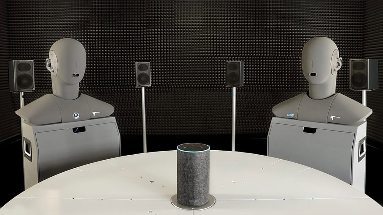 csm_2HMS-II.3-HA-shot A photo sourced from HEAD acoustics of two HMS II.3 head and torso simulators positioned around a smart speaker.