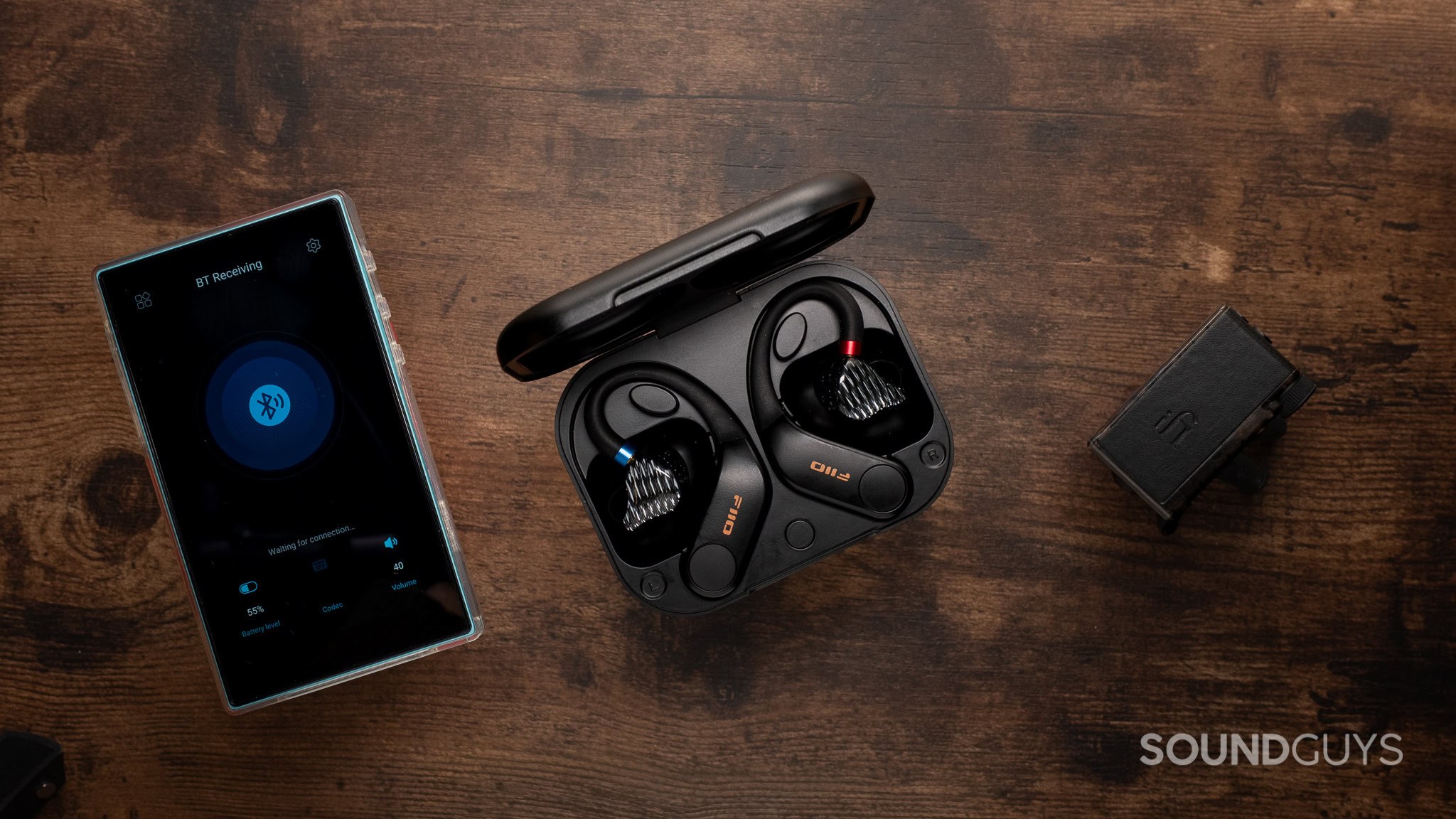 Android device to the left, bluetooth earhook adapters in the center, and a small rectangular 3.5mm jack to Bluetooth adapter.