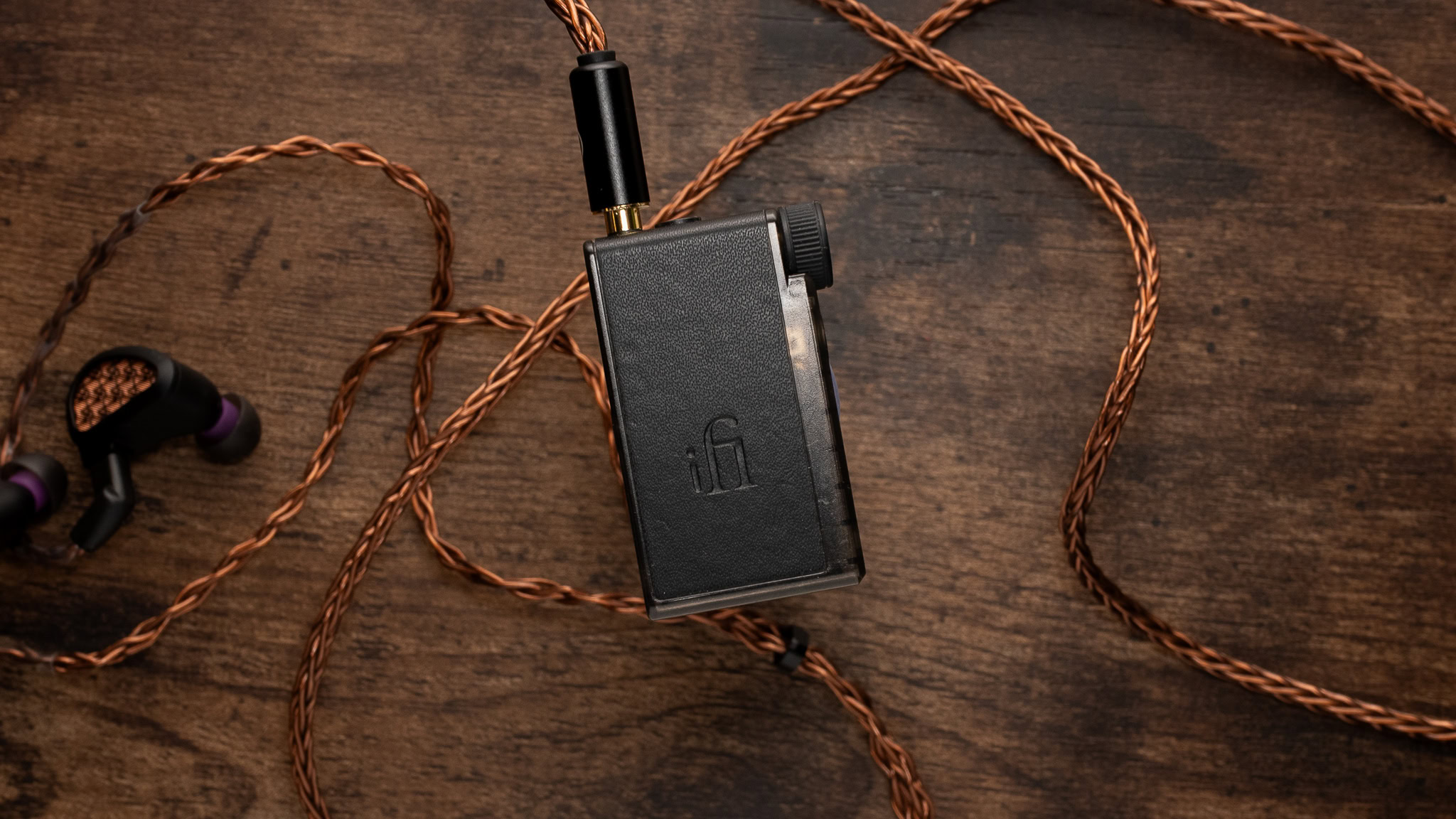 Small rectangular Bluetooth device with wires and earbuds behind it.