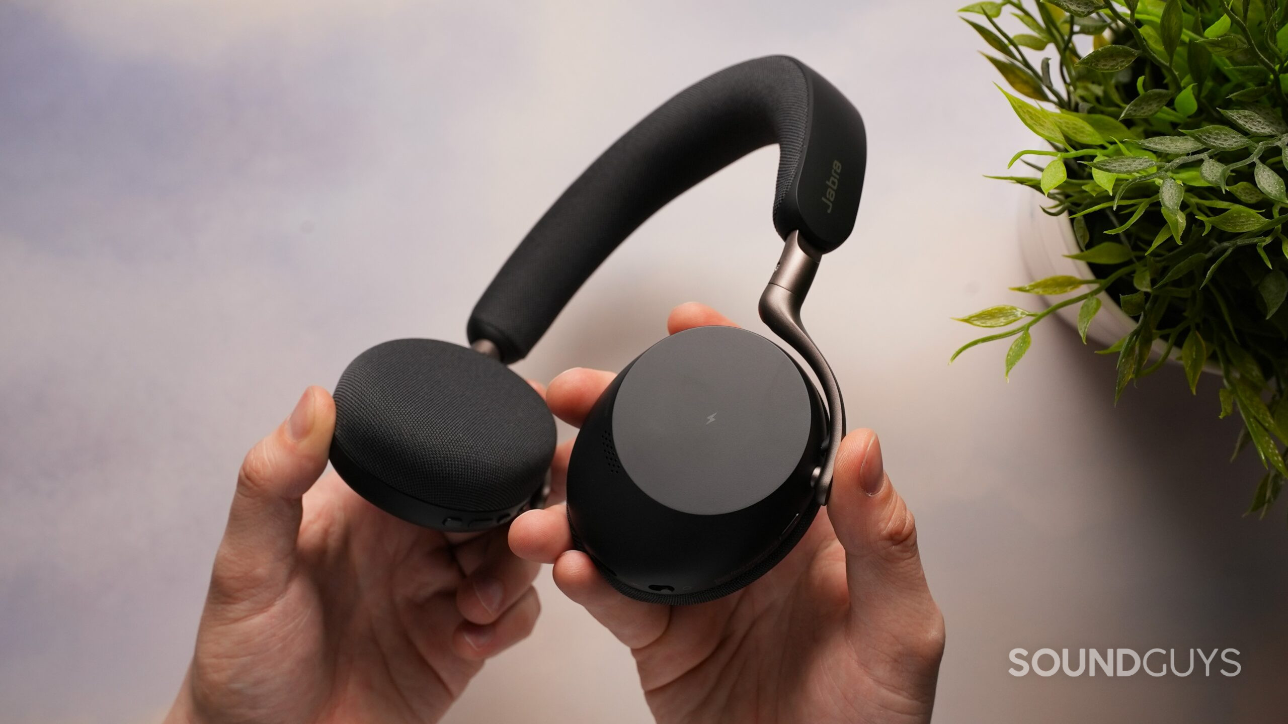 DSC09466 Hands holding Jabra Evolve3 75 black over-ear headphones, showing the compact ear cups, matte finish, and headband design.