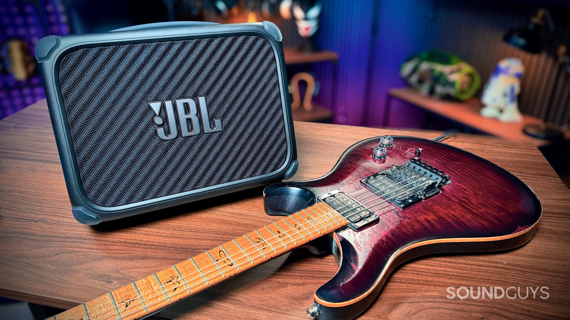 JBL BandBox Trio Studio - 1 (1) The JBL BandBox Trio on a wooden table in the studio with a PRS guitar next to it.