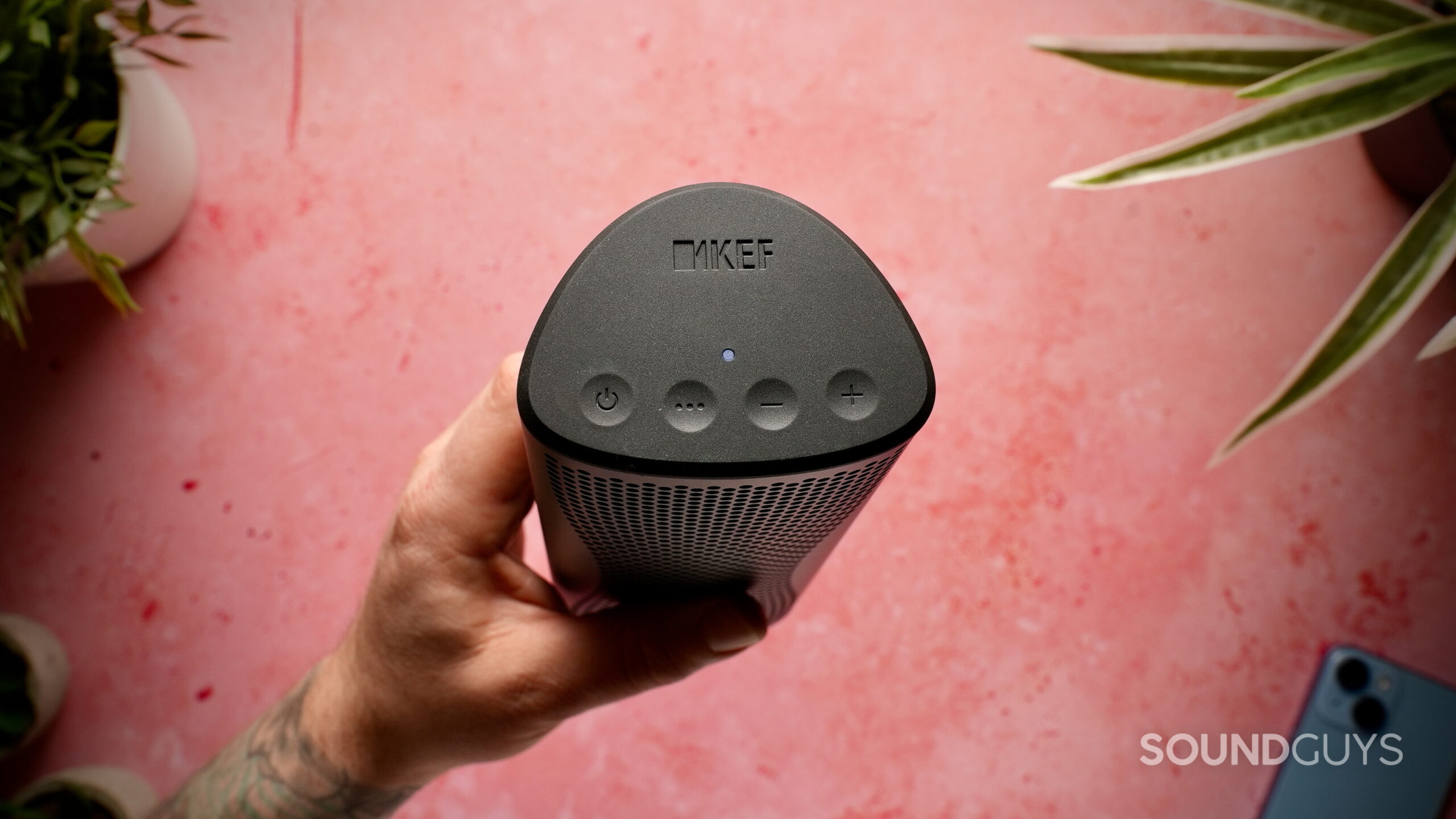 KEF Muo - 3 The KEF Muo Bluetooth speaker in black held in a hand showing the top control buttons and status light.