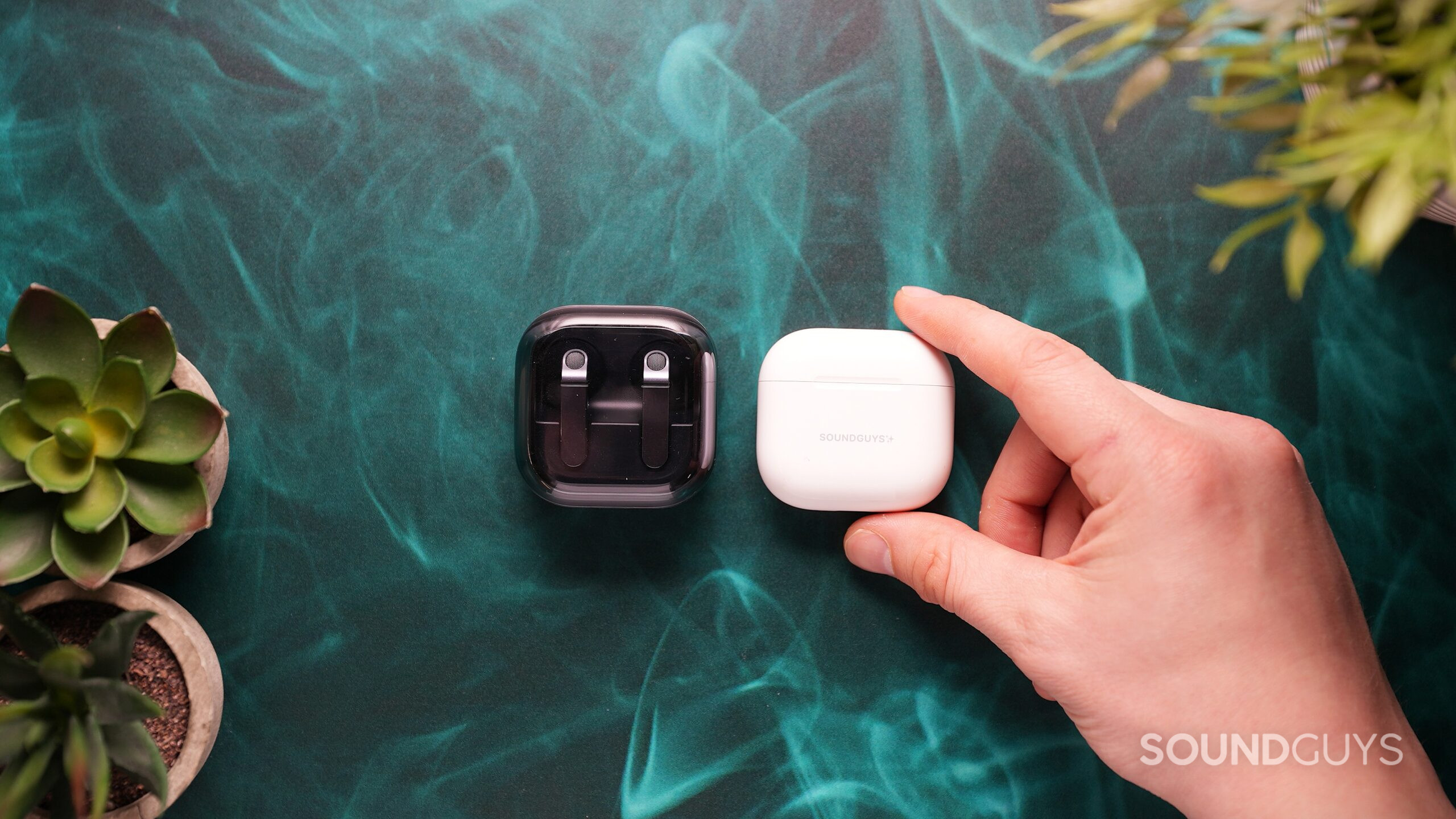 galaxy buds 4 with airpods 4 case the samsing galaxy buds 4 beside a hand holding the apple airpods 4 in case.