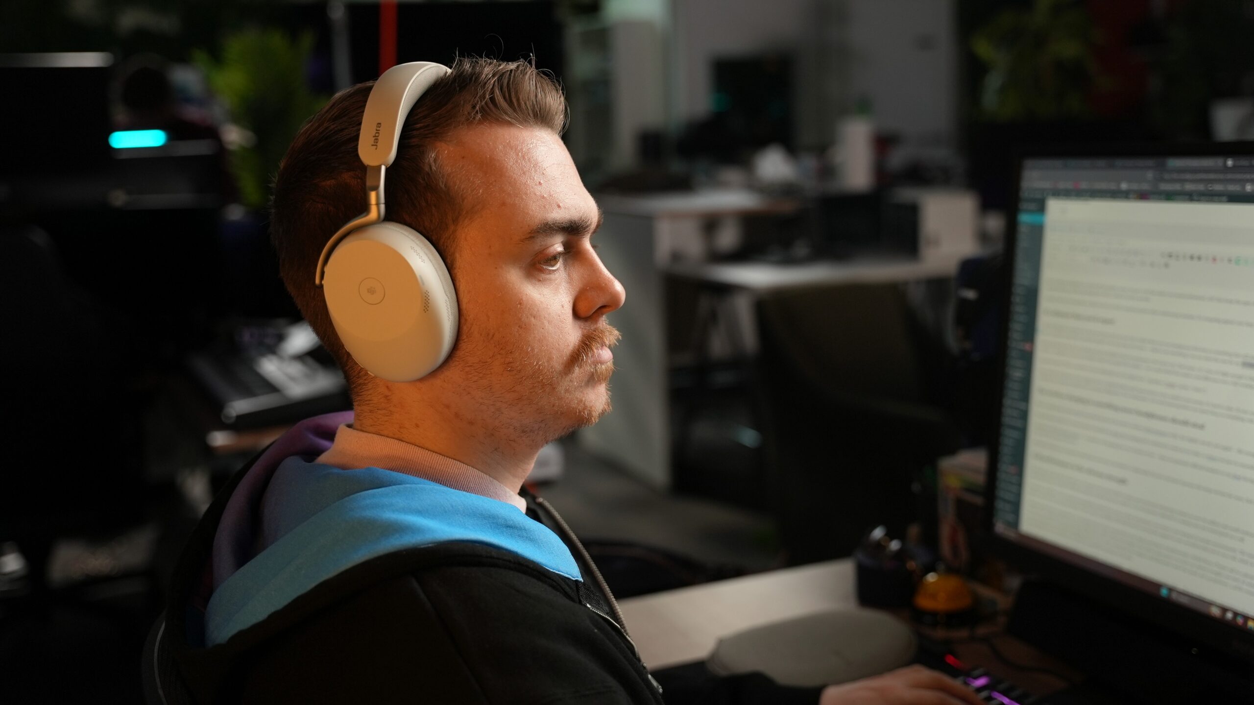 DSC09450 Person wearing Jabra Evolve3 85 white headphones while working at a desk, looking at a computer monitor in a home office setup.