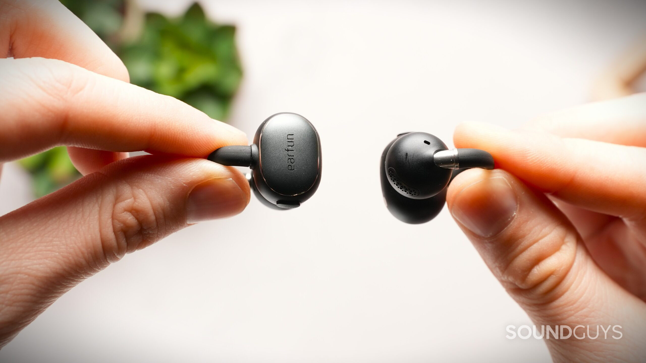 Close-up of two EarFun clip-style earbuds held between fingers, highlighting the speaker grille, microphone port, and matte finish.