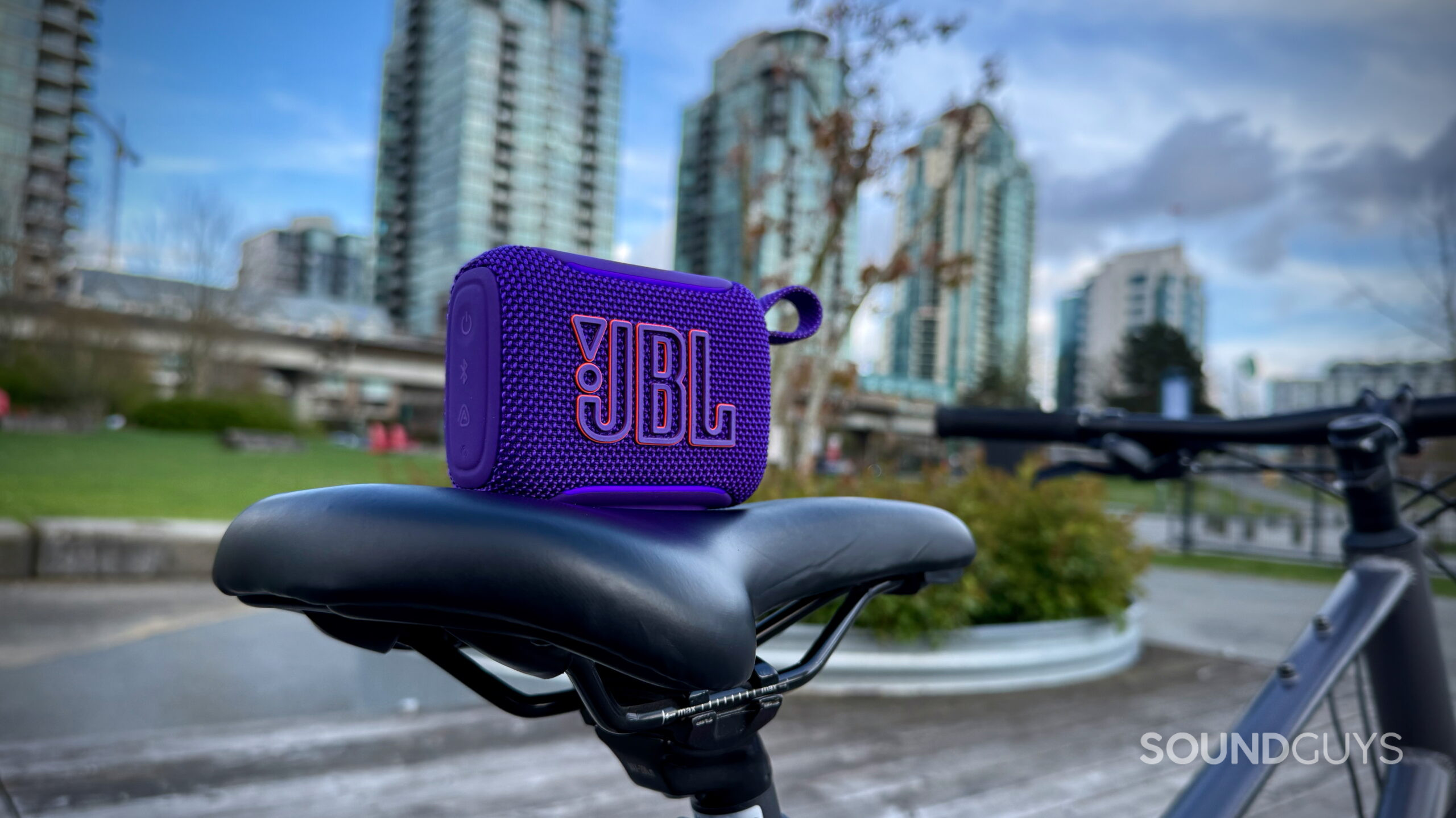 The JBL Go 5 is placed on a bicycle seat with an urban skyline behind it