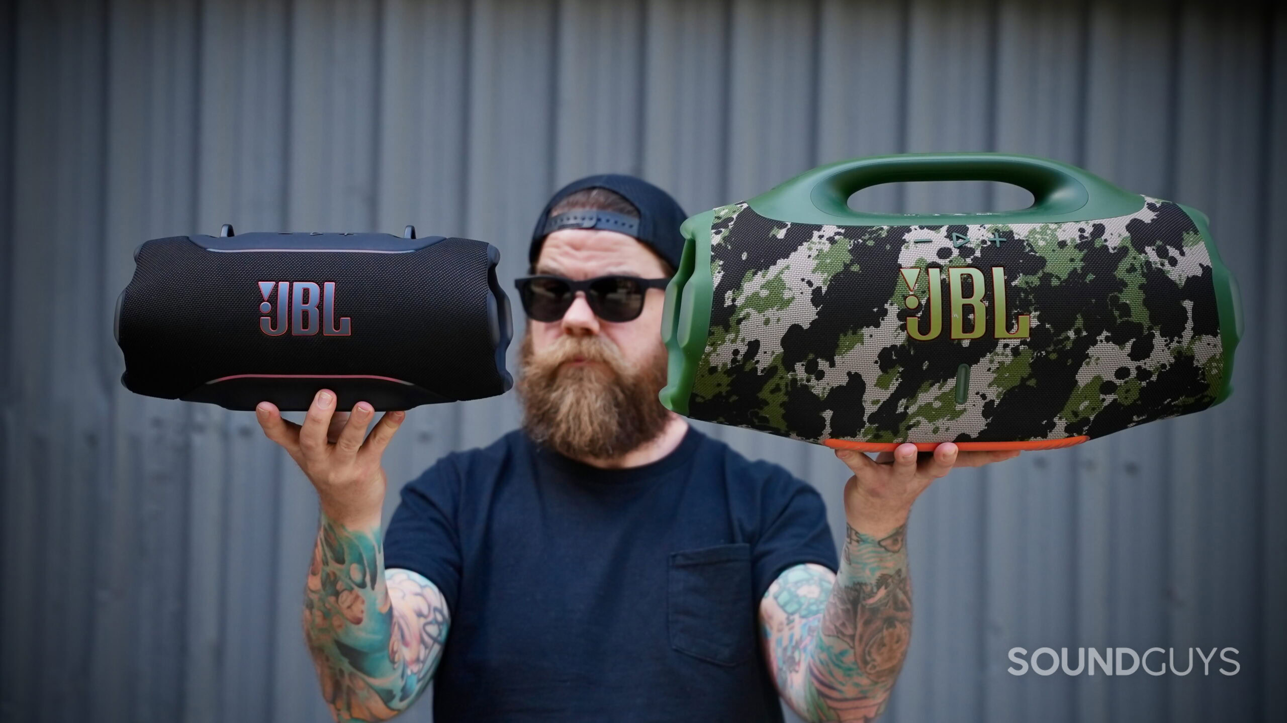 Person holding the JBL Xtreme 5 in one hand and JBL Boombox 4 in the other for direct size comparison.