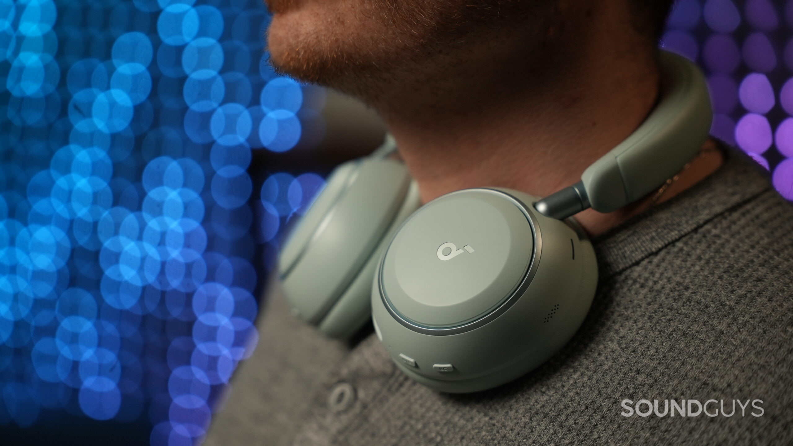 anker soundcore space 2 on neck Soundcore Space 2 headphones resting around a man’s neck, showing earcup design and control buttons against a blurred blue light background.