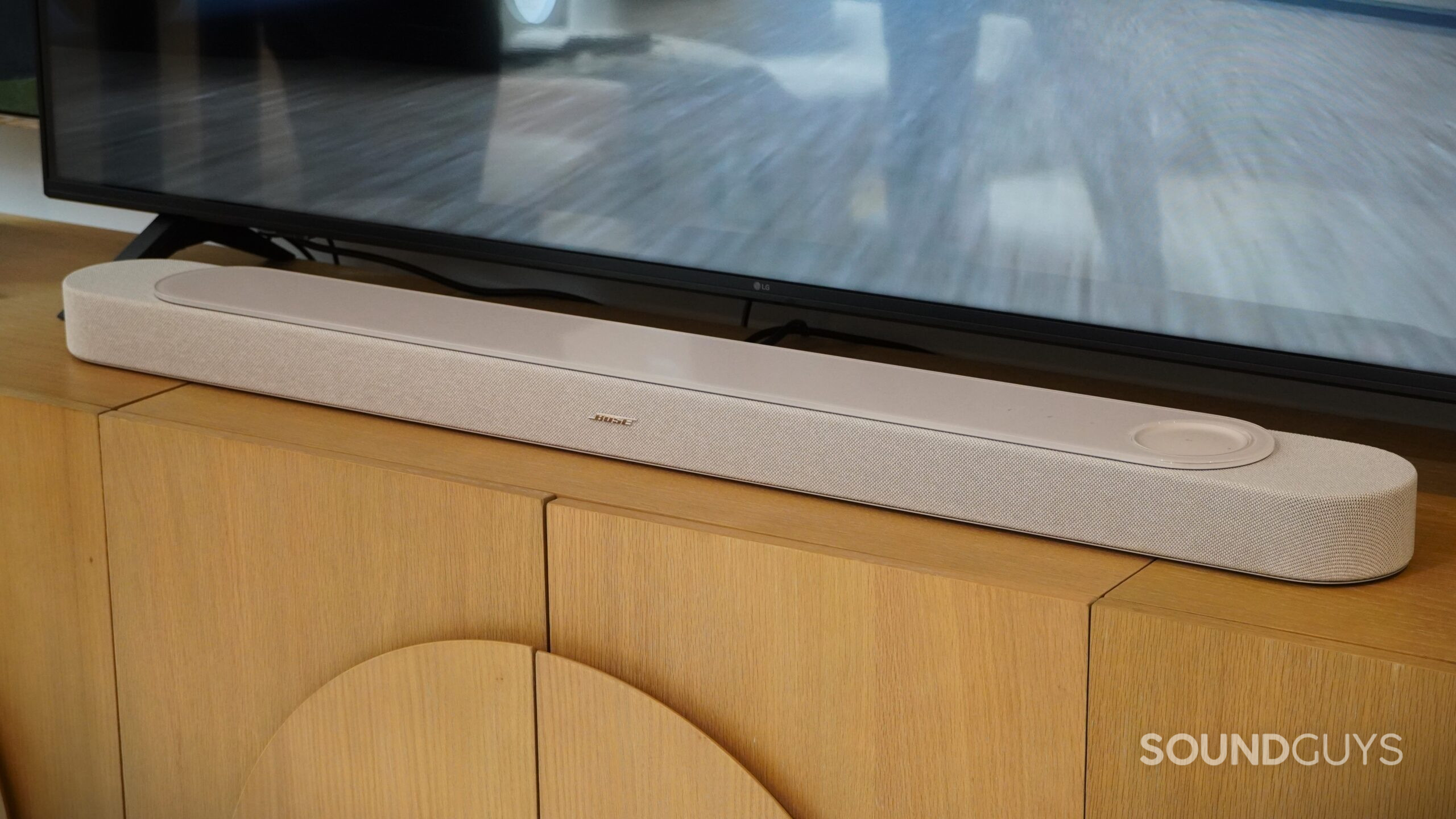 Bose LifeStyle Ultra Soundbar Bose soundbar placed on a wooden media console beneath a flat-screen TV.