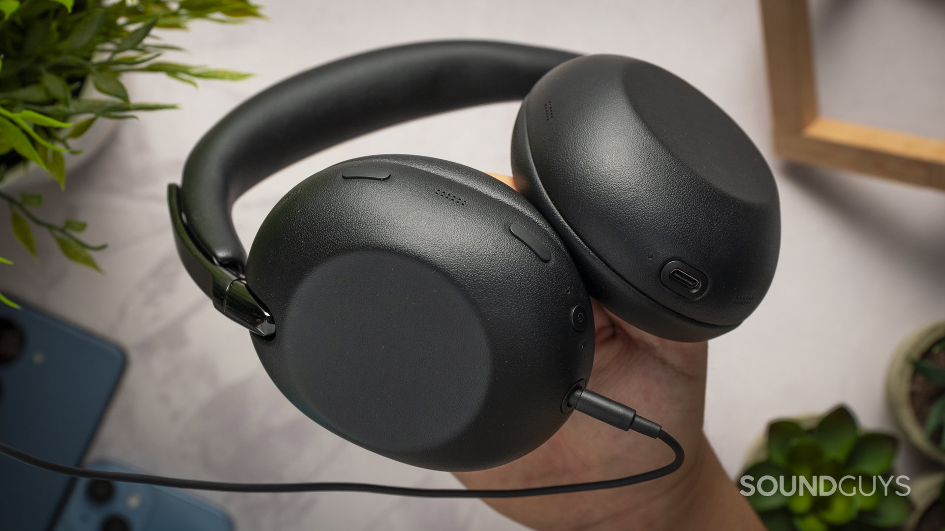A photo of the Sony WH-1000XX the Collexion being held in someone's hand, with the 3.5mm TRS cable plugged in.
