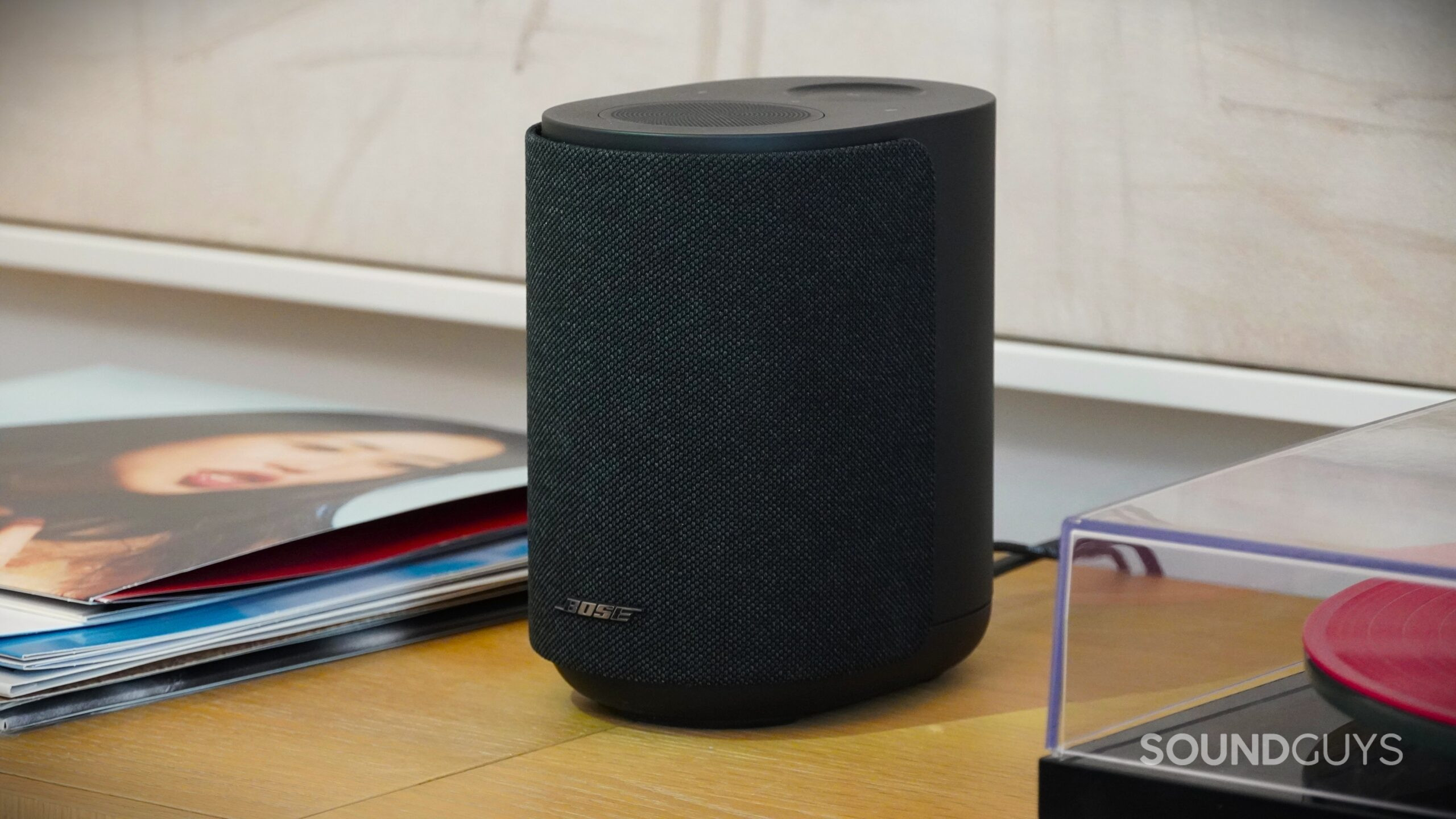 Black Bose smart speaker on a wooden surface next to stacked vinyl records.