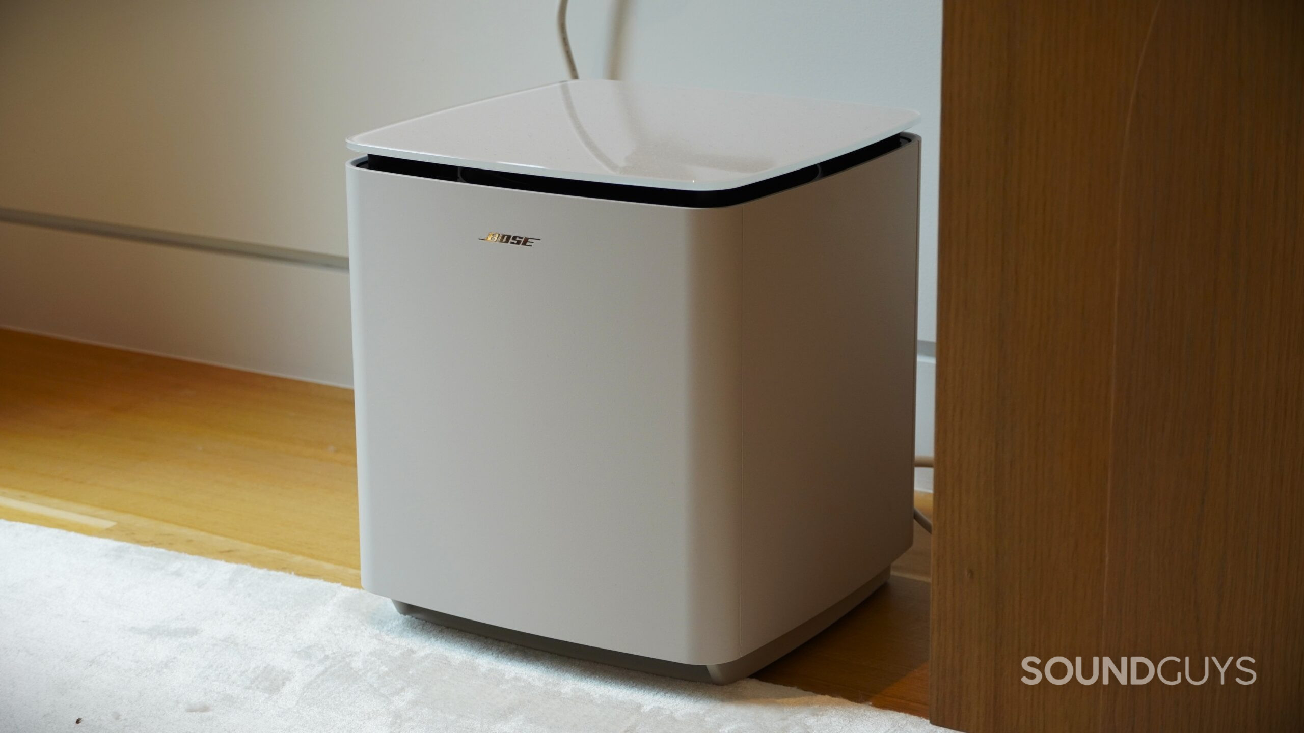 Bose subwoofer placed on the floor beside a cabinet, featuring a sleek cube design.