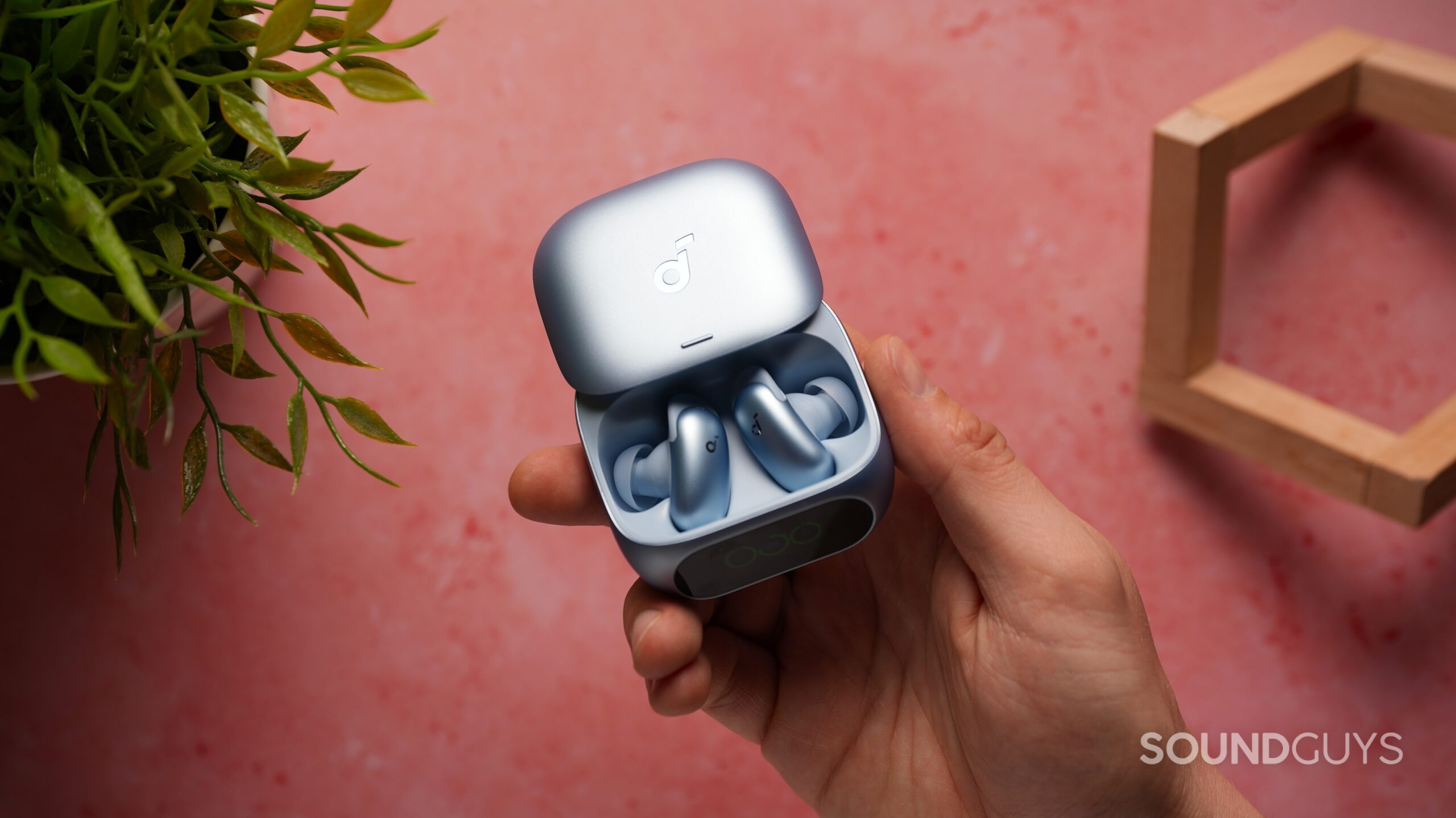 Person holding the open Soundcore Liberty 5 Pro charging case with both earbuds visible inside against a pink background.