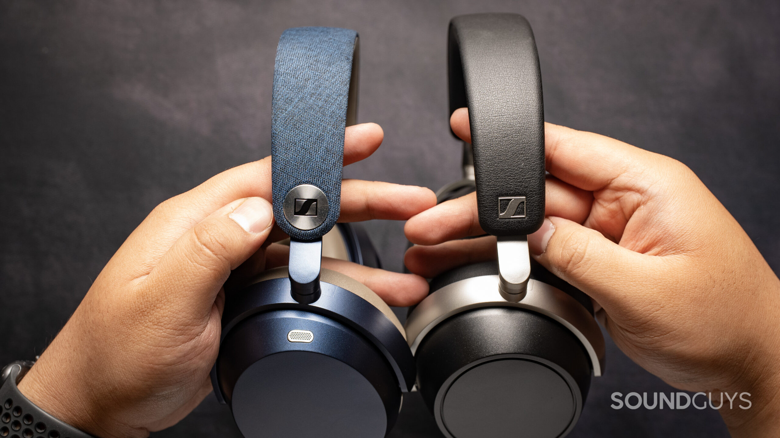 sennheiser momentum 5 wireless headphones vs. sennheiser hdb 630_side A photo of the Sennheiser MOMENTUM 5 Wireless held next to the Sennheiser HDB 630. The bands of each are prominently visible, showing the fabric of the former against the leatherette of the latter.