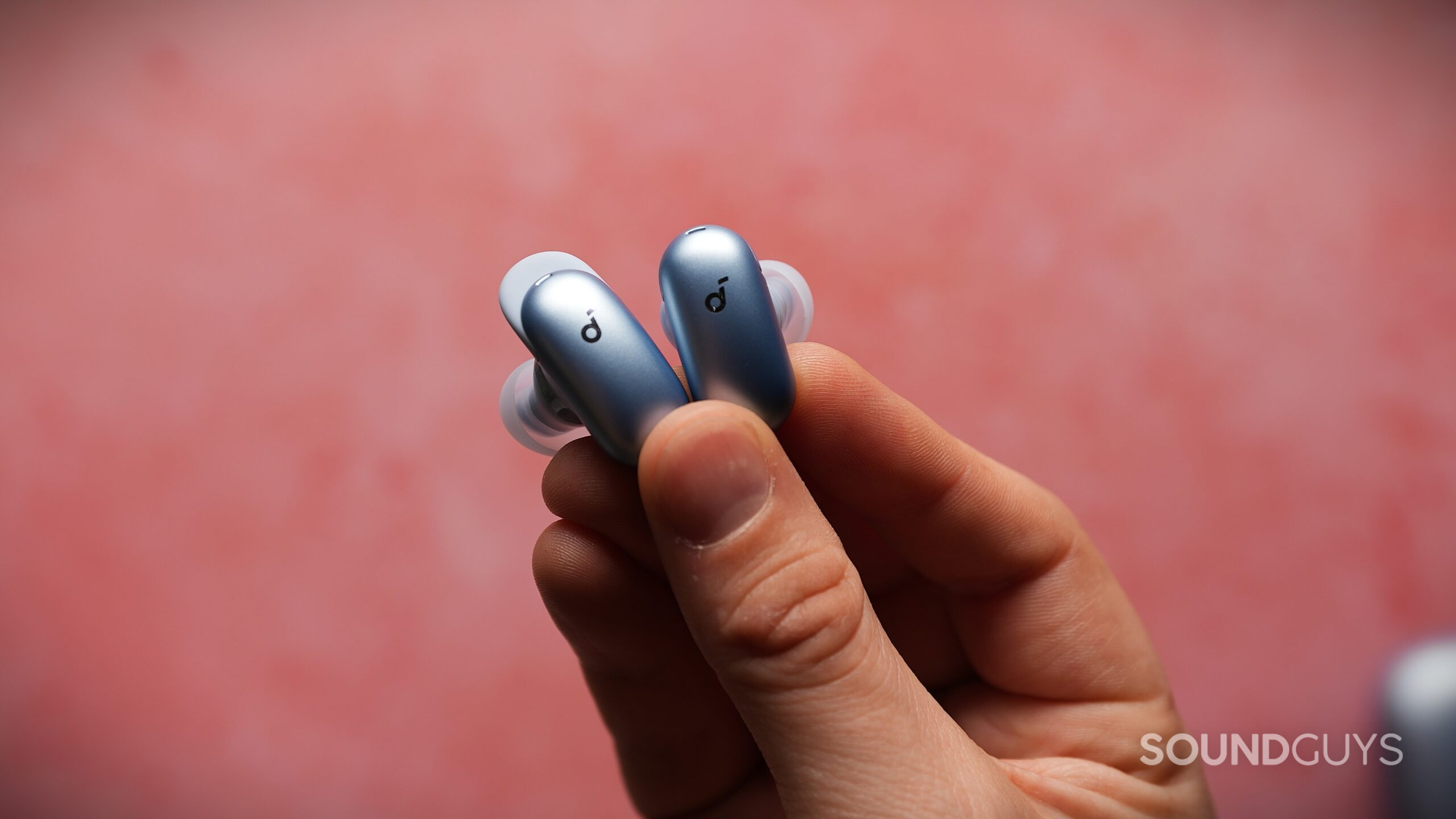 soundcore liberty 5 pro ear fin Close-up of two blue Soundcore Liberty 5 Pro wireless earbuds held between fingers, showing the curved ear fin design and silicone ear tips.