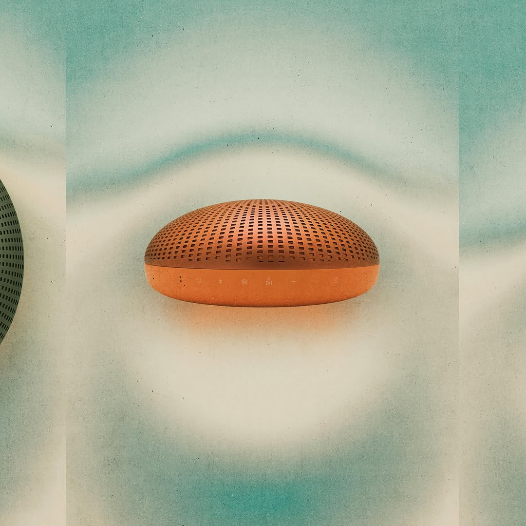 Side profile of a bronze portable speaker floating against a soft blue and cream gradient background, showing its curved silhouette and control panel.